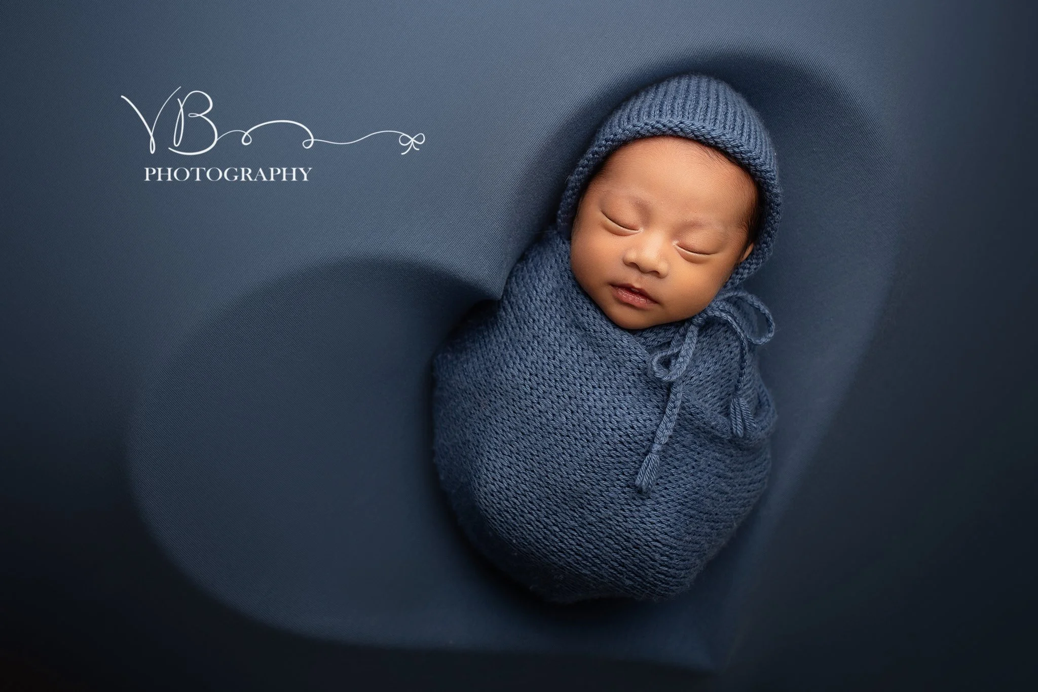 Sleeping newborn wrapped in wool blanket posed in heart prop during studio session