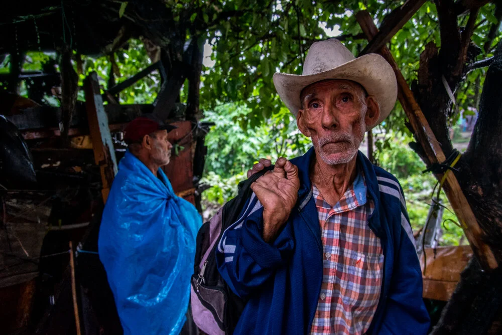  Two men with homes in danger of being swept away by an overflowing river keep cover under a tree while watching the river rise.  The aftermath of Hurricane Eta brings enormous amounts of rainfall which will cause deadly flooding and mudslides throug