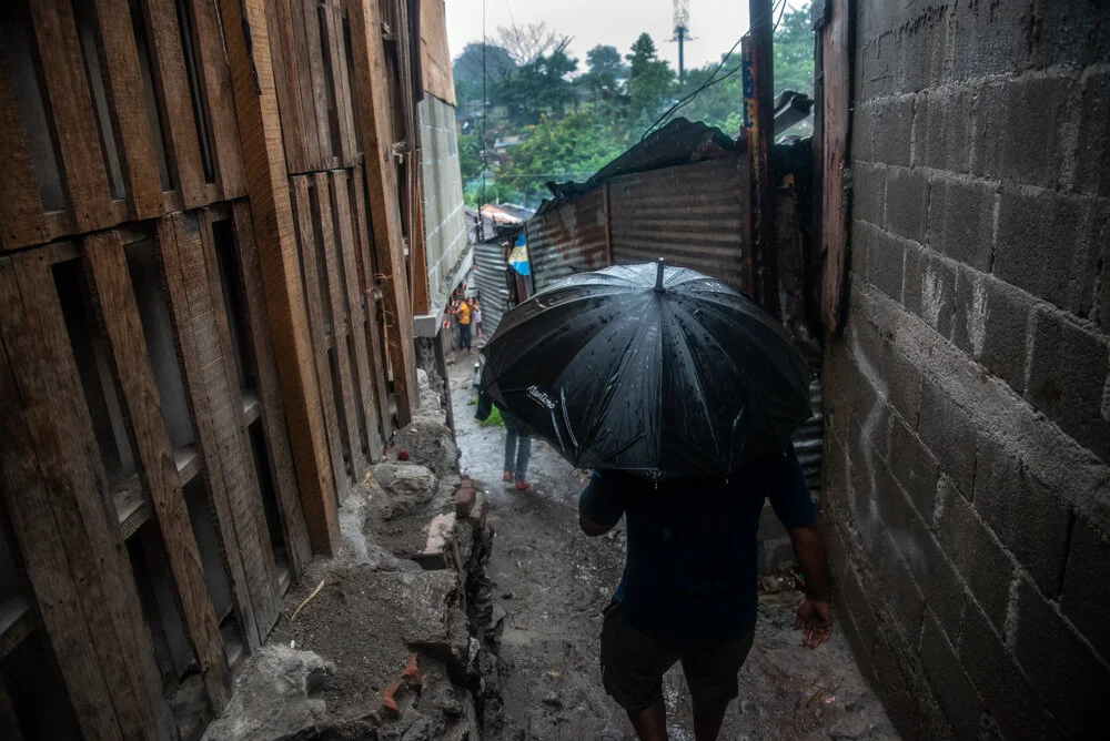  A man with an umbrella navigates through the slim alleys of a shanty village in San Pedro Sula, which is in danger of being swept away by the adjacent overflowing river--the after effects of Hurricane Eta. The aftermath of Hurricane Eta brings enorm