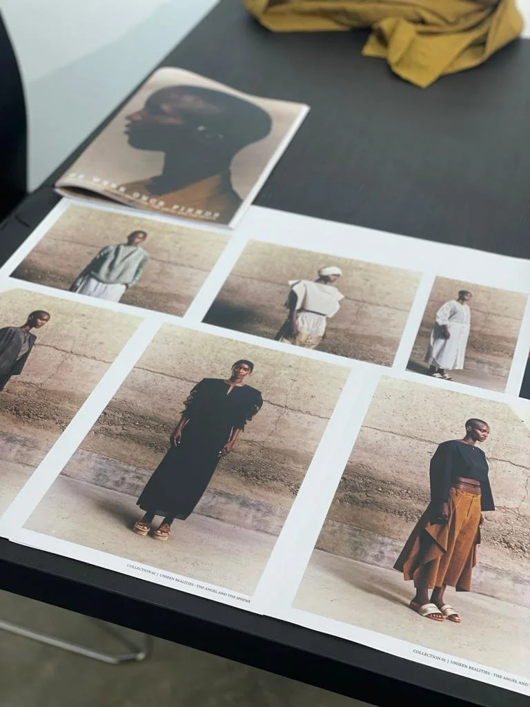 Fashion photographs on a table showcasing diverse models in stylish outfits, with a magazine featuring a profile silhouette on top.