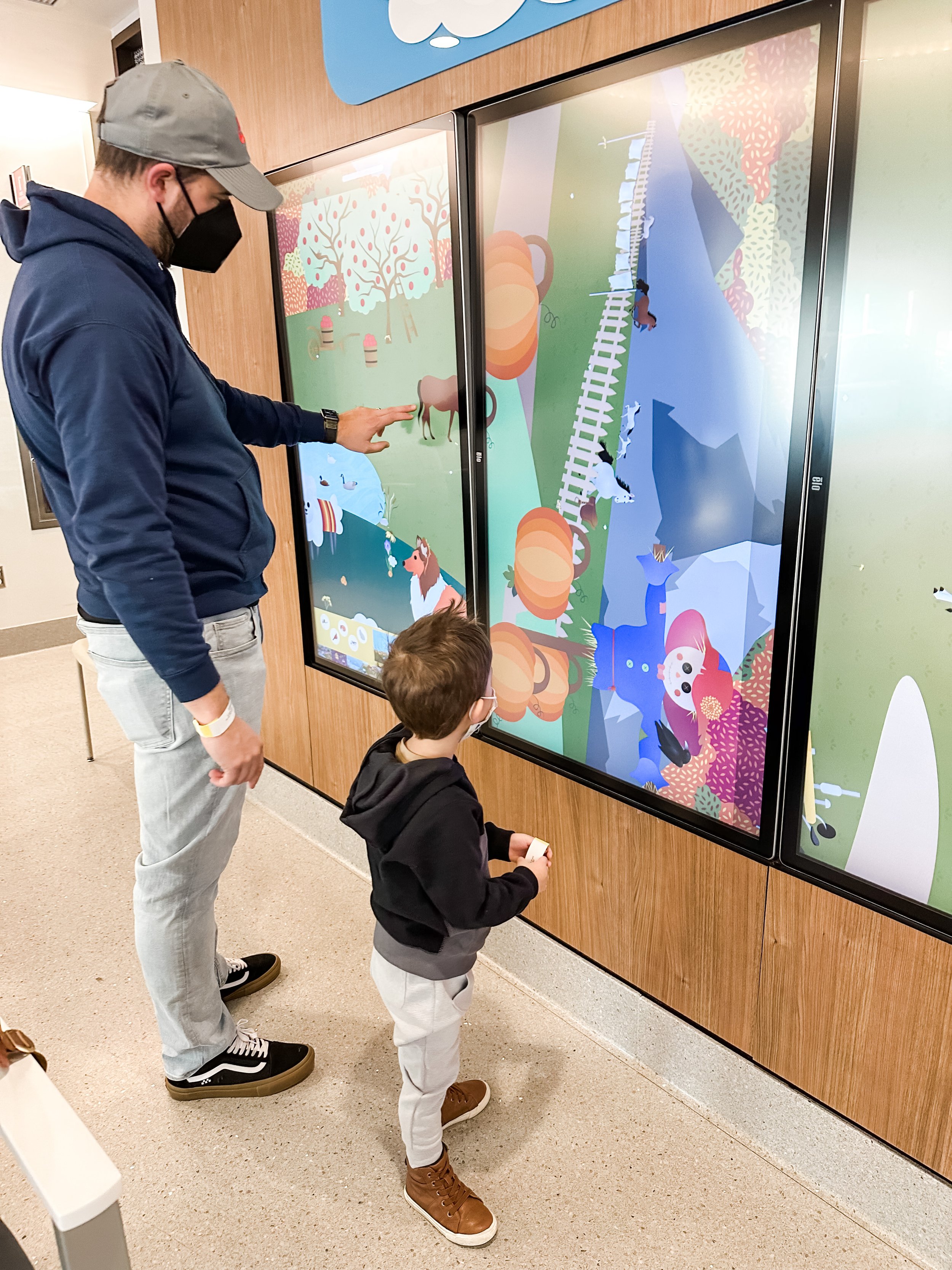  father and son looking at touchscreen tvs in hospital waiting room 