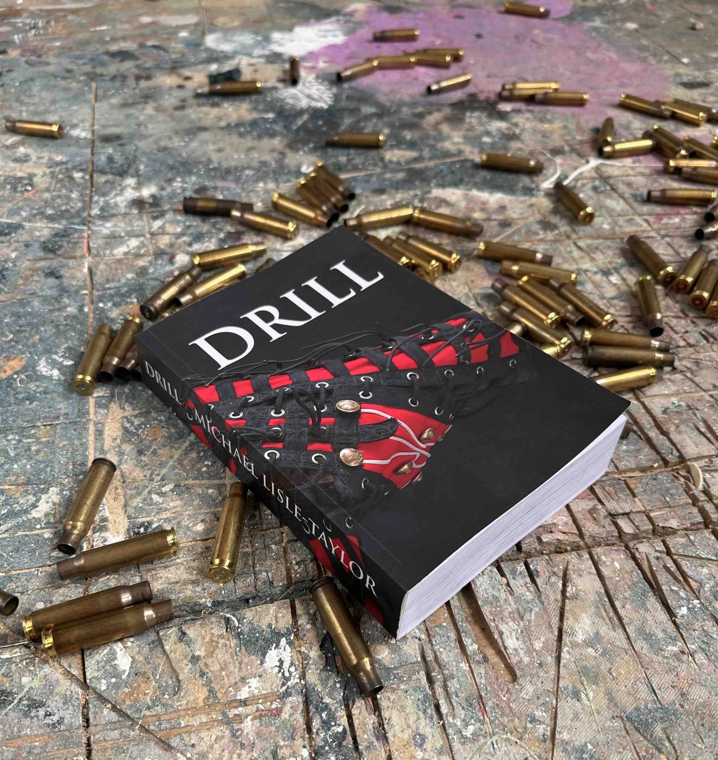 Image of Michael Lisle-Taylor's book titled 'Drill' resting on a paint splattered and scored artist's studio floor