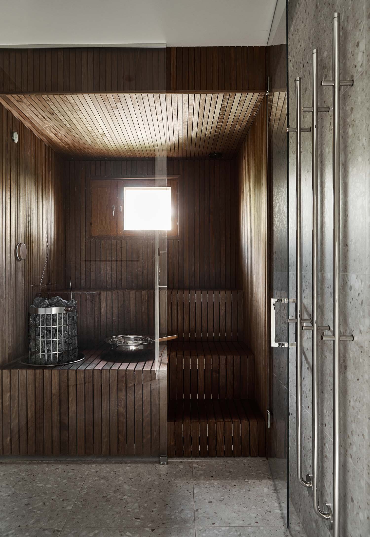 Nykyaikainen puinen sauna, jossa on puiset lauteet, kiuas kivillä ja pieni ikkuna.