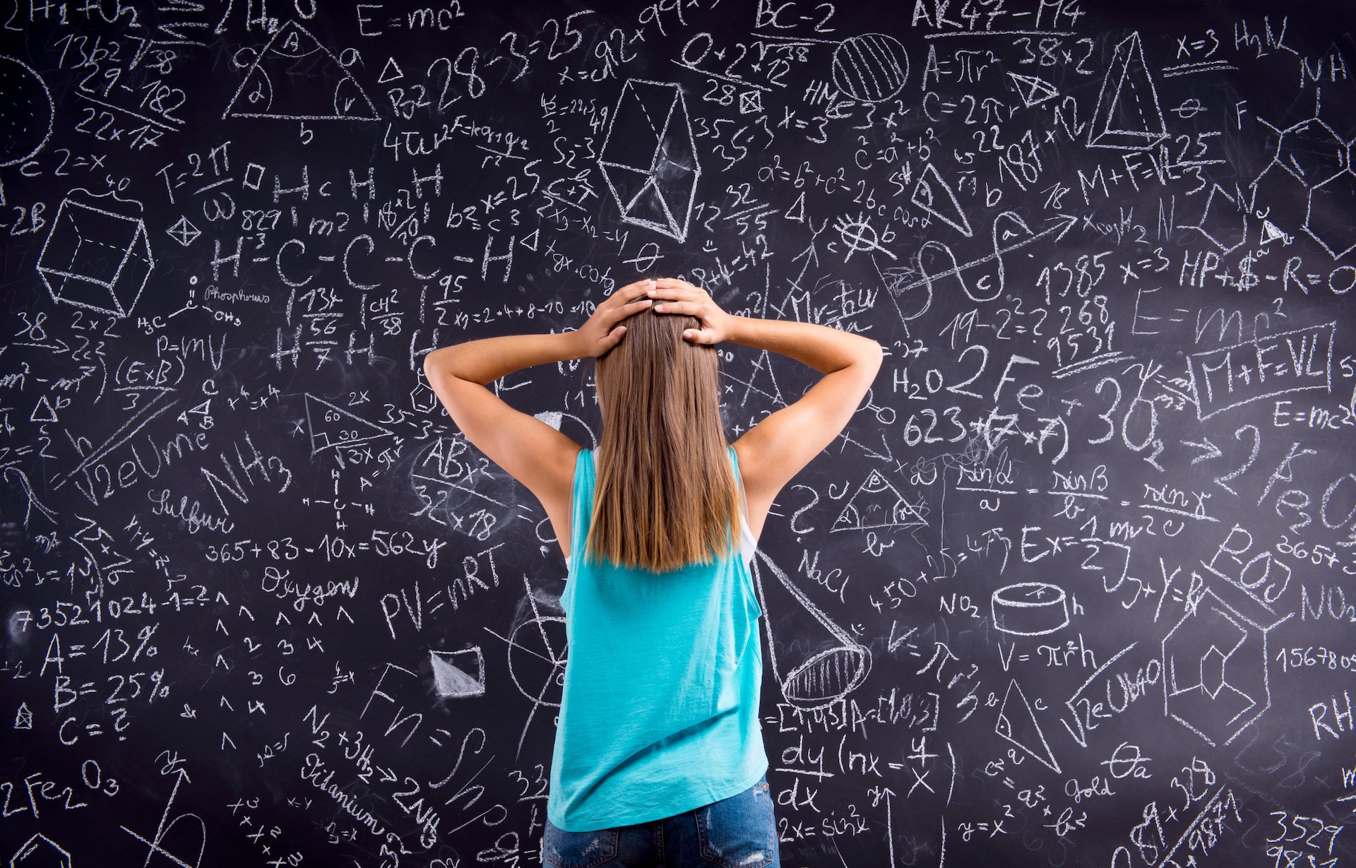 thinking-girl-in-blue-singlet-holding-her-head-against-big-blackboard-with-mathematica-SBI-305194228.jpg
