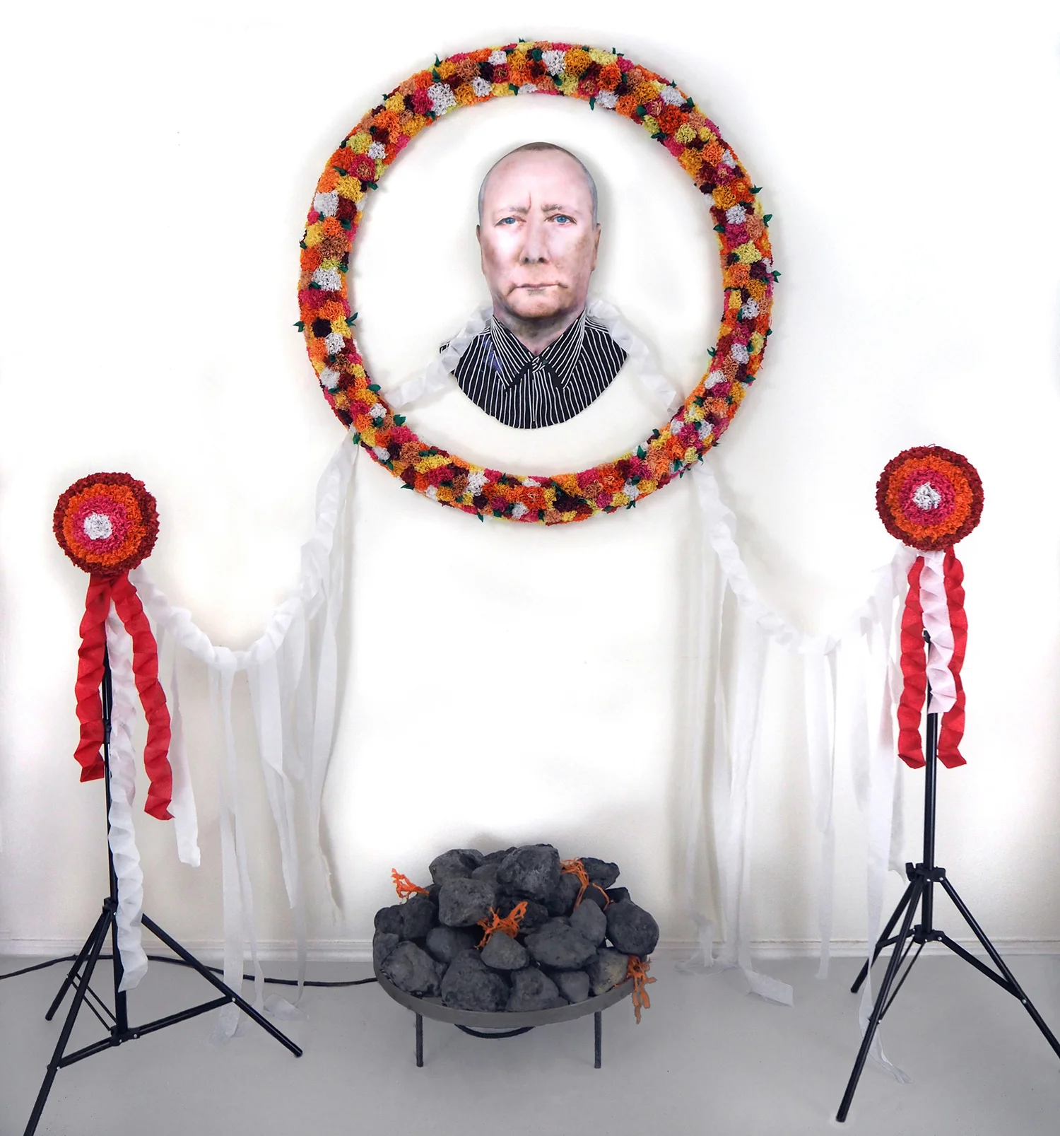 Carrie Fonder, Portrait of an Artist as a Dead Man , 2016, Urethane foam, tissue paper, streamers, steel, yarn, airbrushed acrylic, 80 x 85 x 46 inches This mixed media sculptural installation features an airbrushed acrylic portrait of artist Mike Kelley. A tissue paper wreath, streamers, and urethane foam rocks surround the portrait and are activated by a concealed fan.