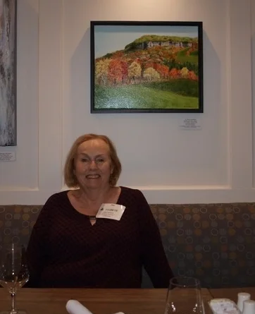 Helen seated for lunch in front of her painting.