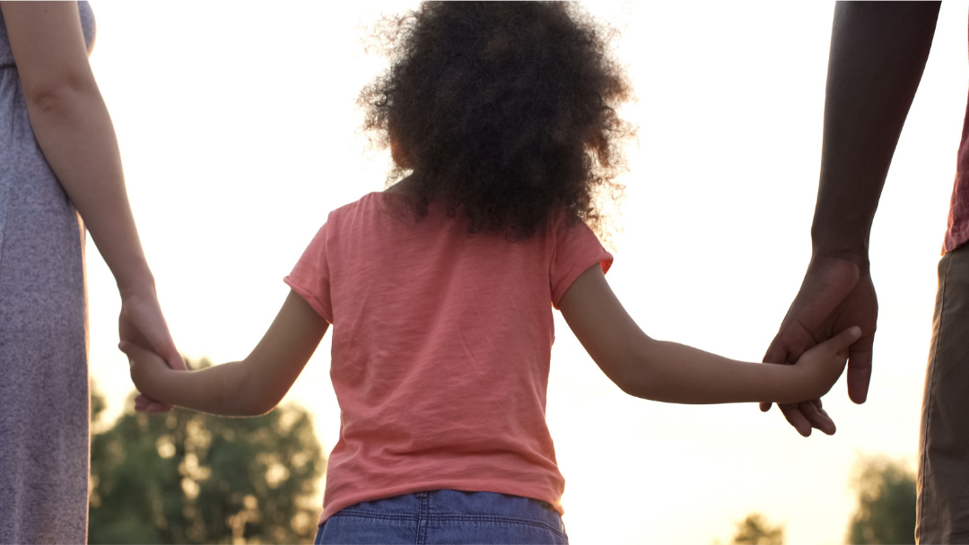 African American little girl holding the hands of a white mom and black father