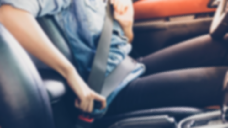 Person fastening a seatbelt while seated behind the wheel of a car