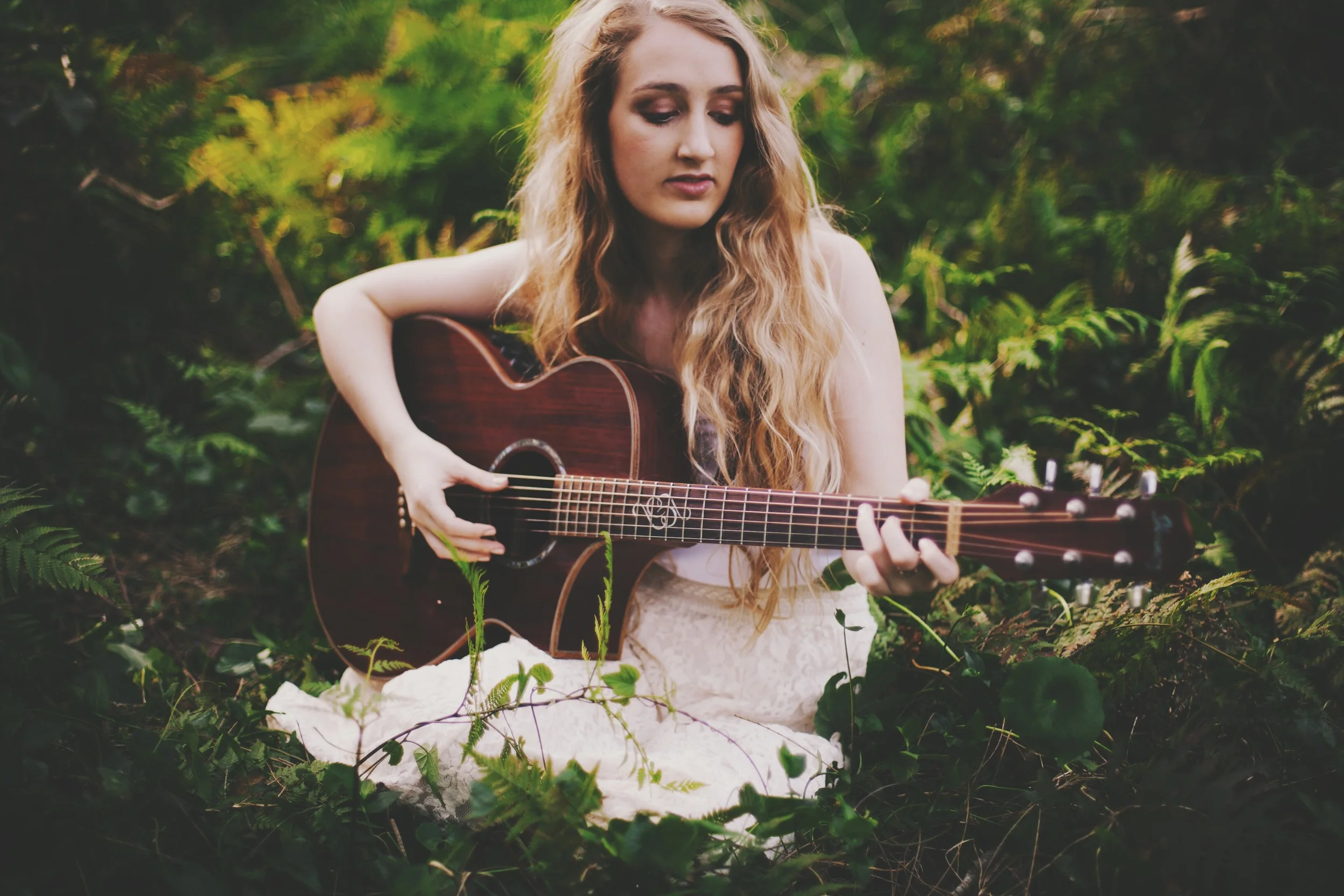 girl sitting in a field of wheat with guitar