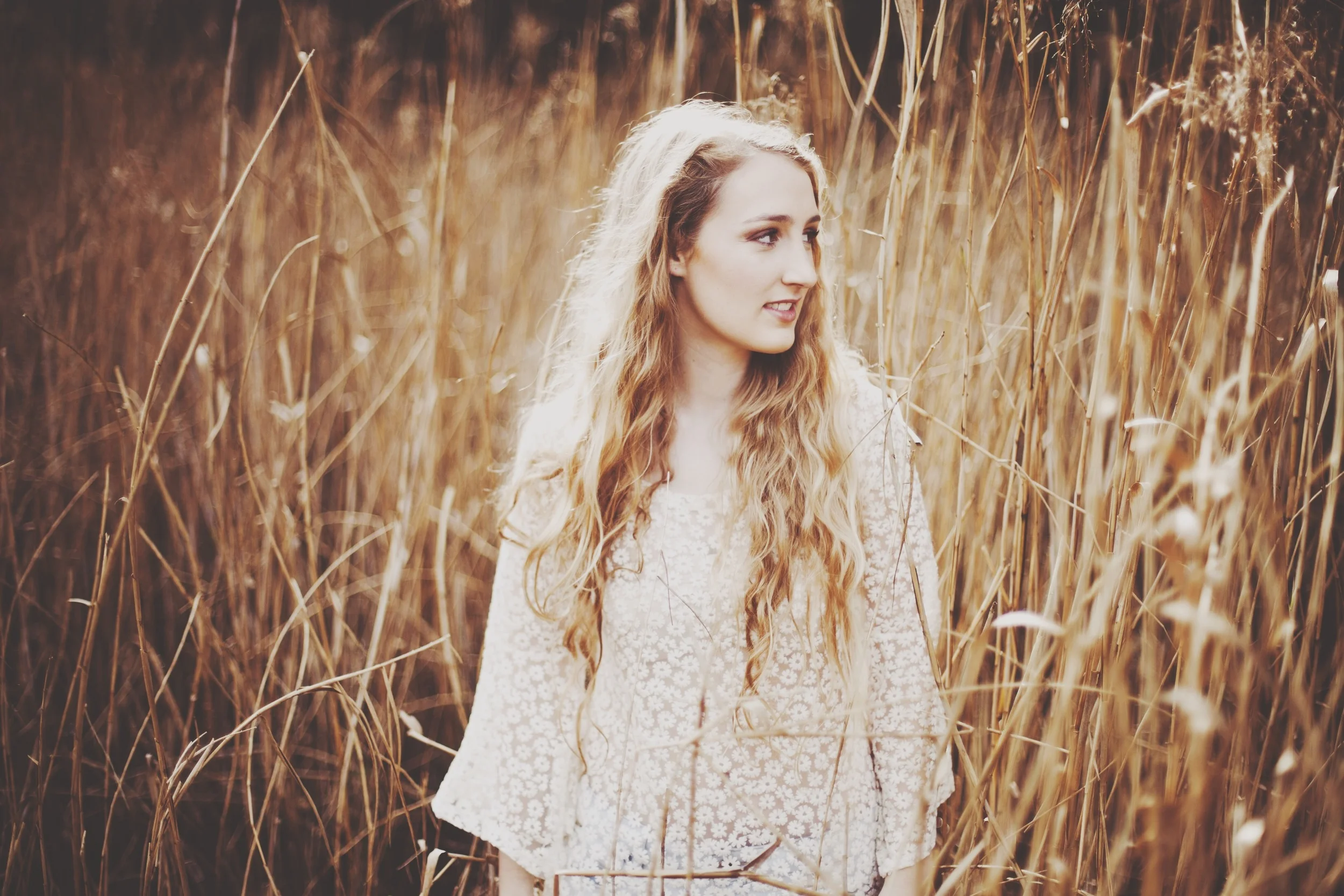 girl sitting in a field of wheat with guitar