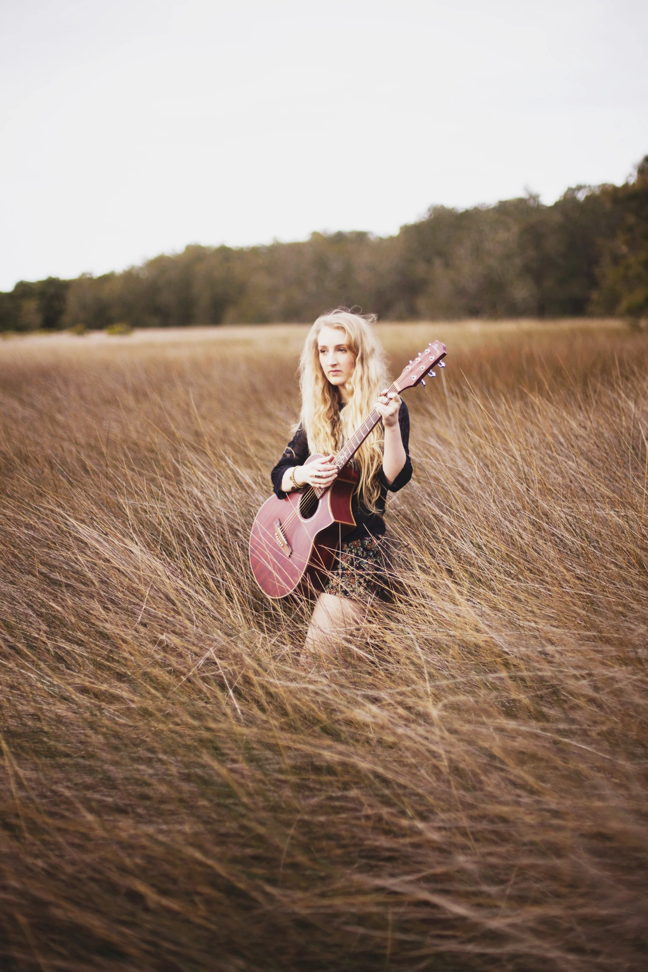 girl sitting in a field of wheat with guitar