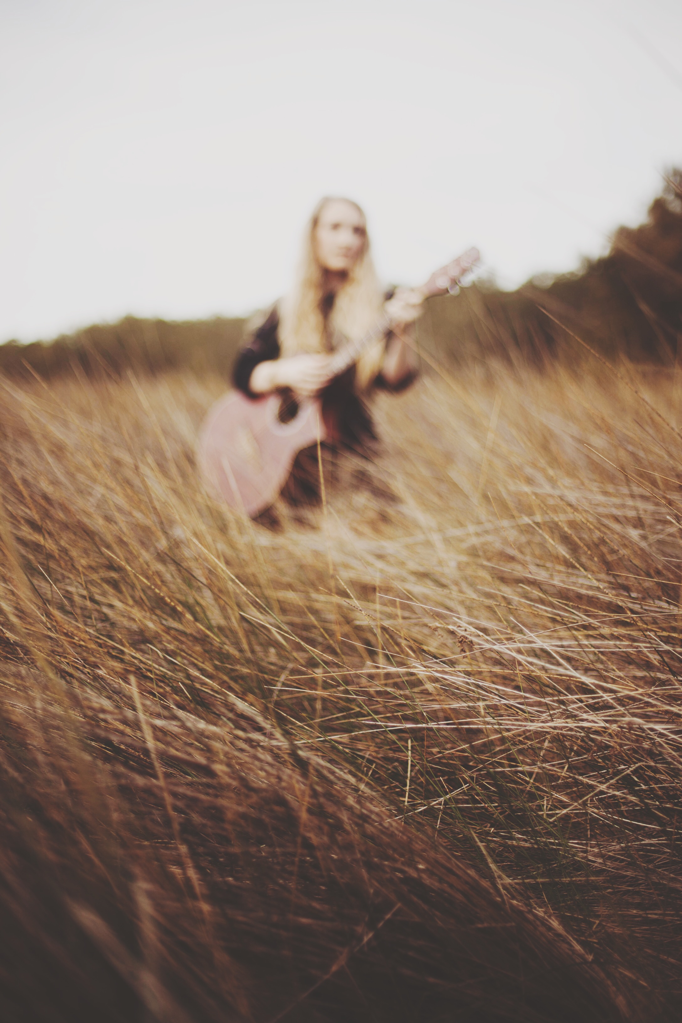girl sitting in a field of wheat with guitar
