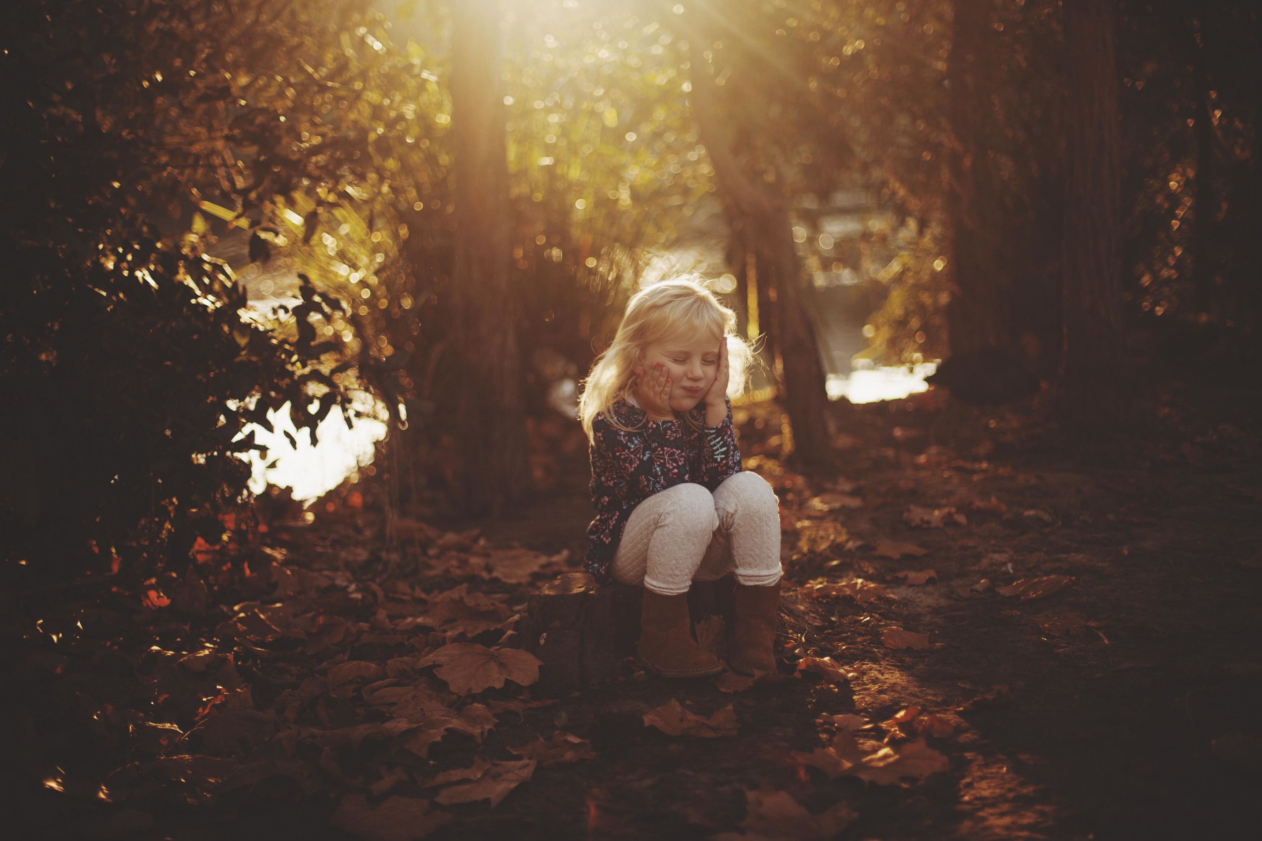 young girl sitting amongst the autumn leaves at sunset 