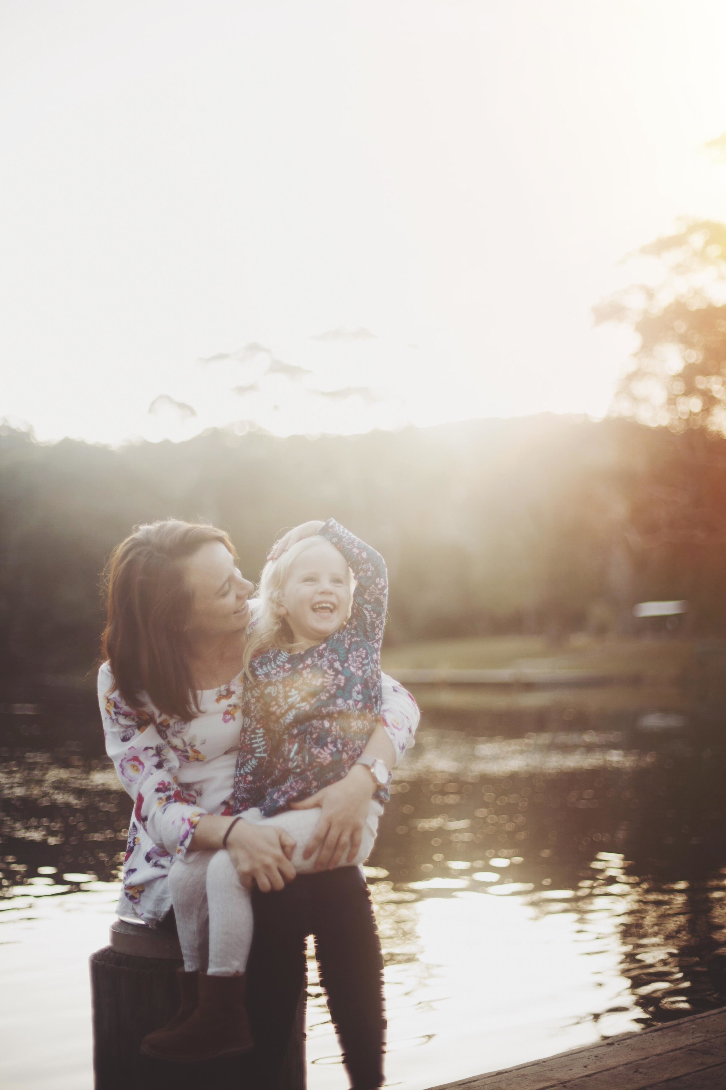mother and daughter laughing together at sunset by the water