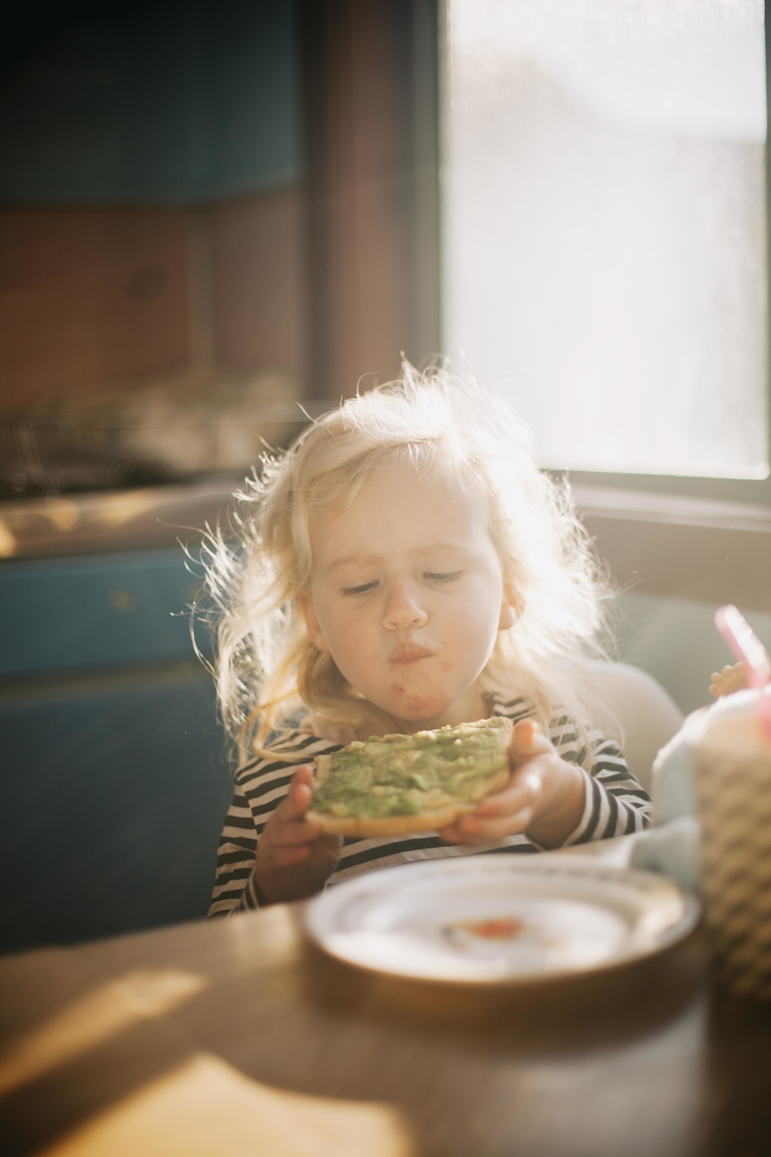 young girl sitting at kitchen table eating avocado toast for breakfast 