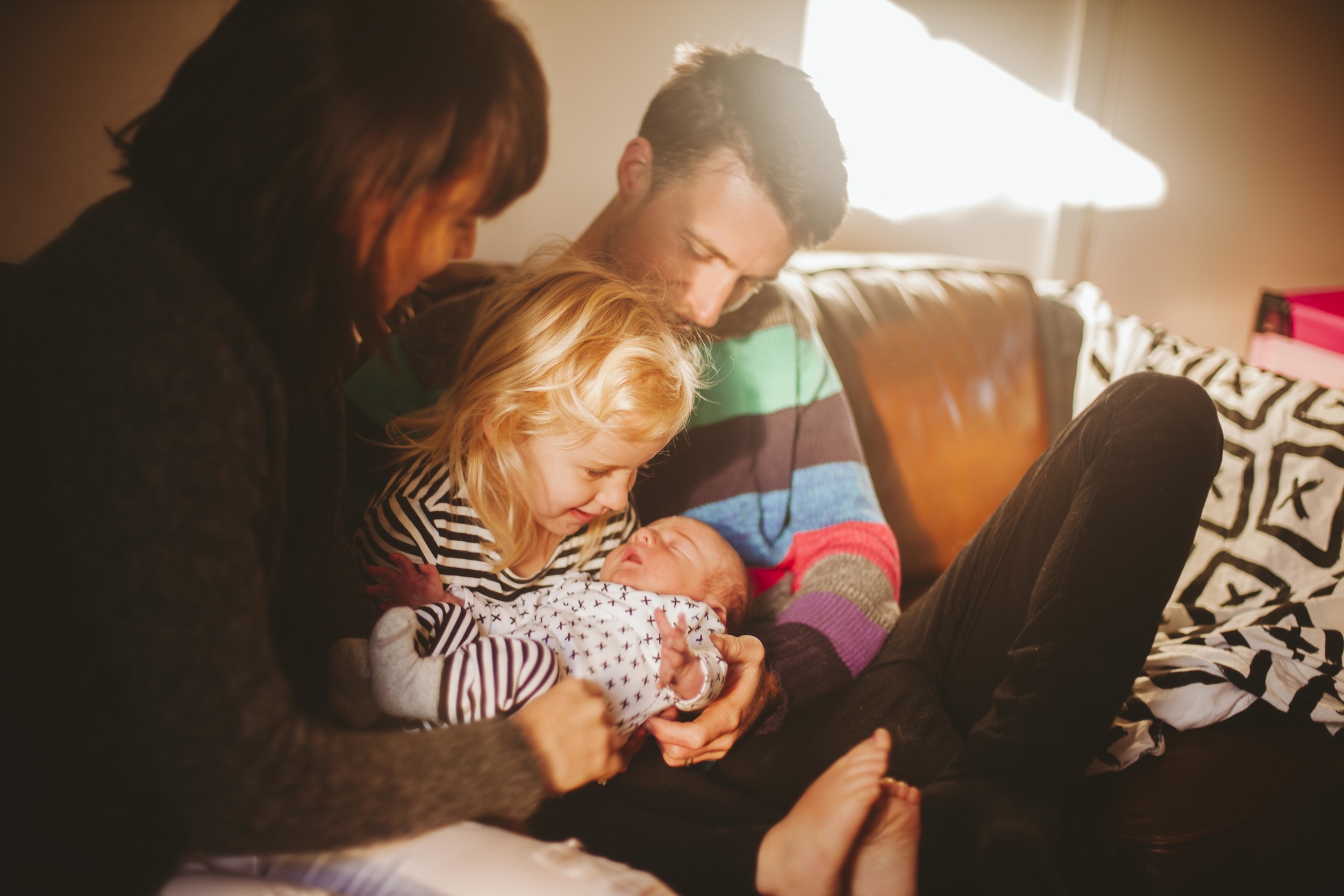 family laughing on couch looking at newborn son