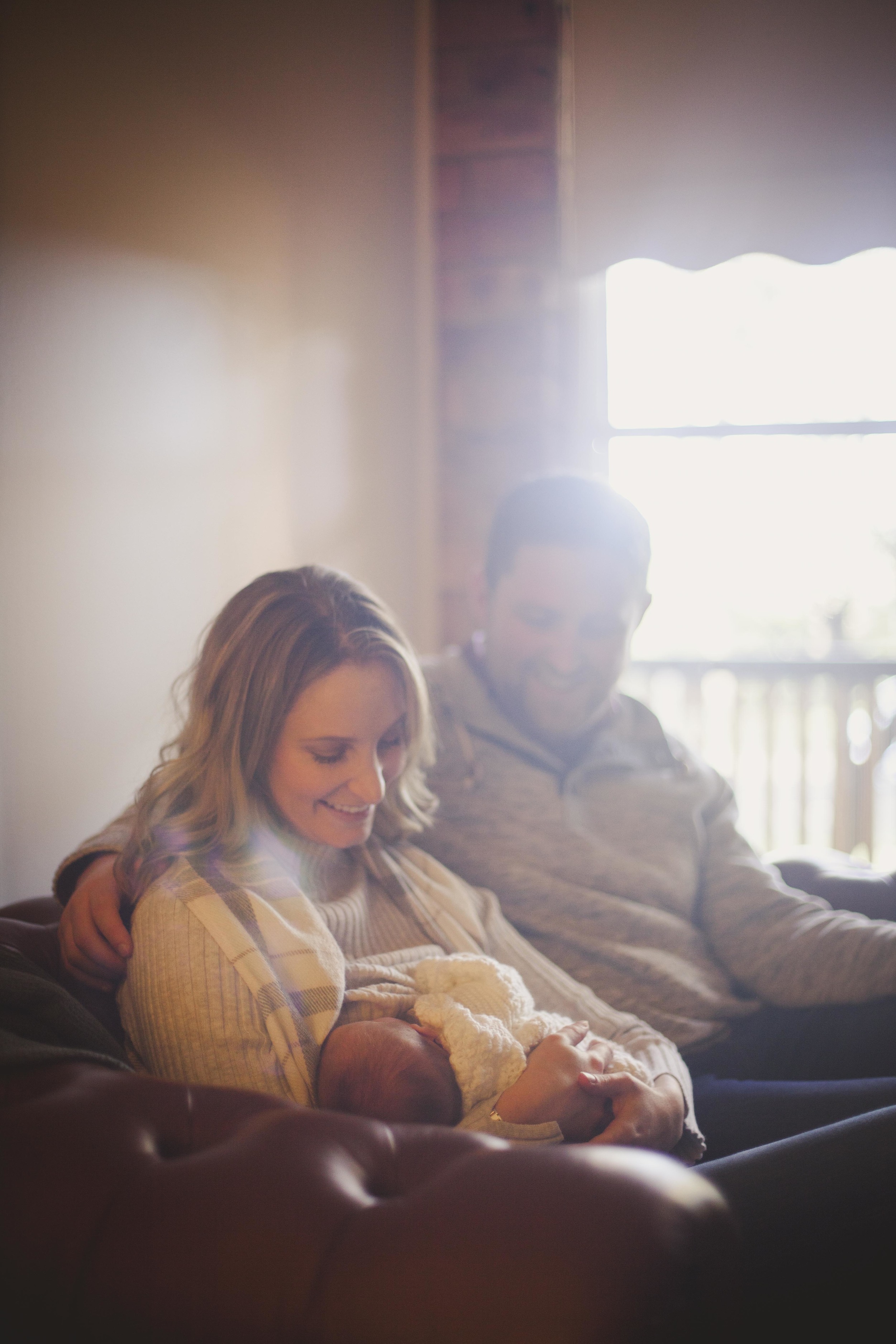 parents sitting on couch smiling at newborn baby