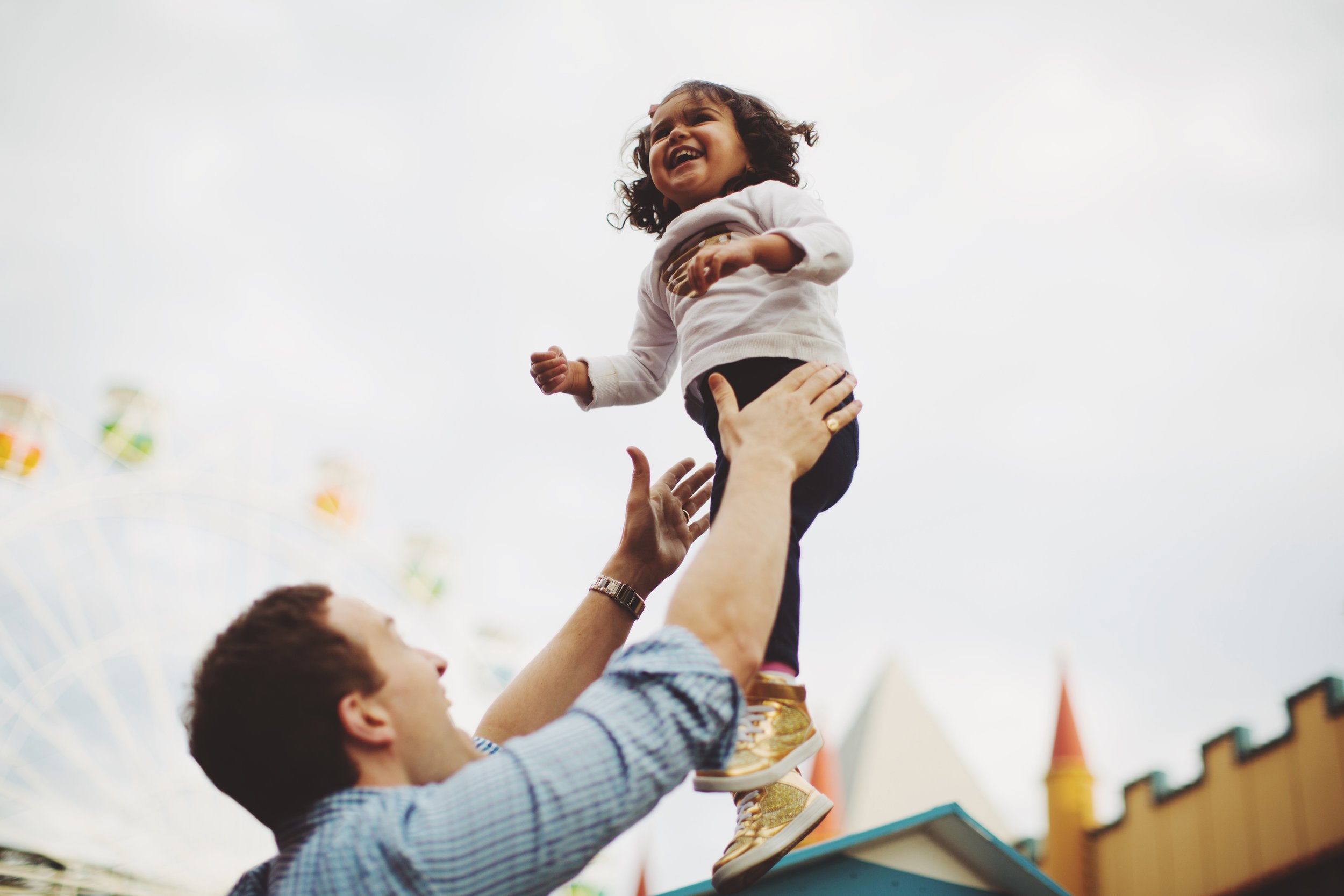 father lifting young girl into the air at luna park in syndey