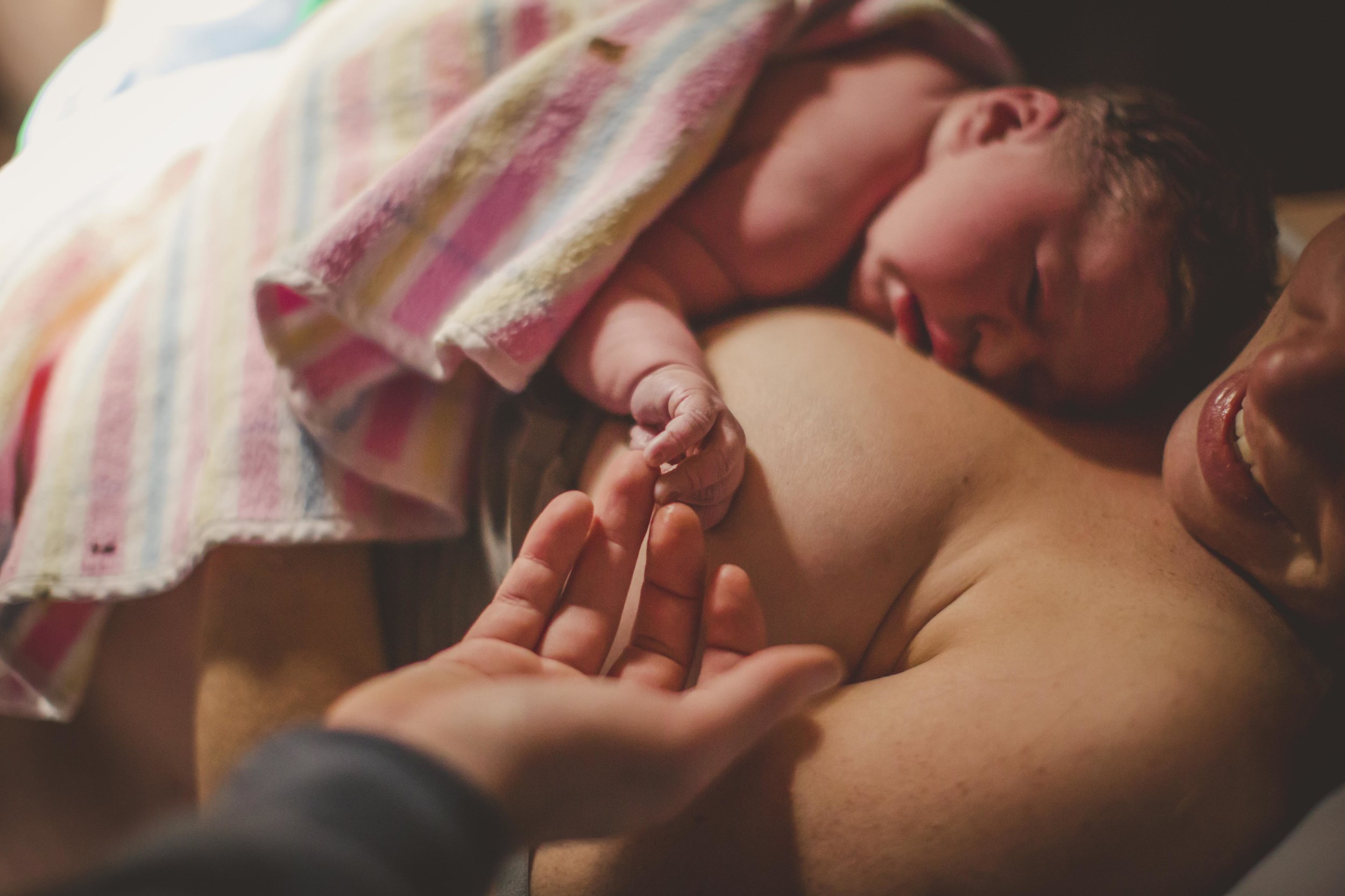 newborn resting on mother's chest after birth hand reaching out to touch baby's hand