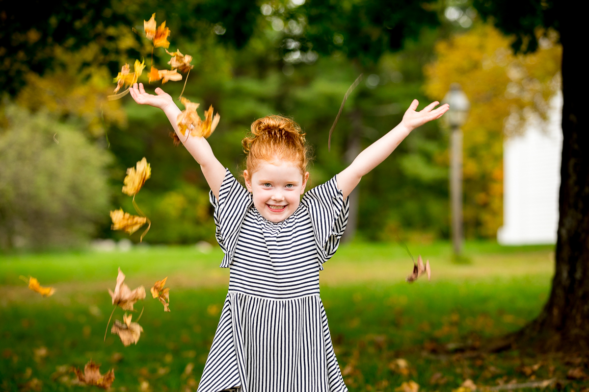 Fun photo of a young girl throwing leaves in the air during a family photo session in Sudbury MA