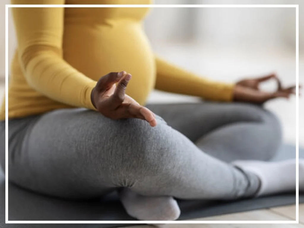 Pregnant woman sitting crossed legged doing prenatal yoga