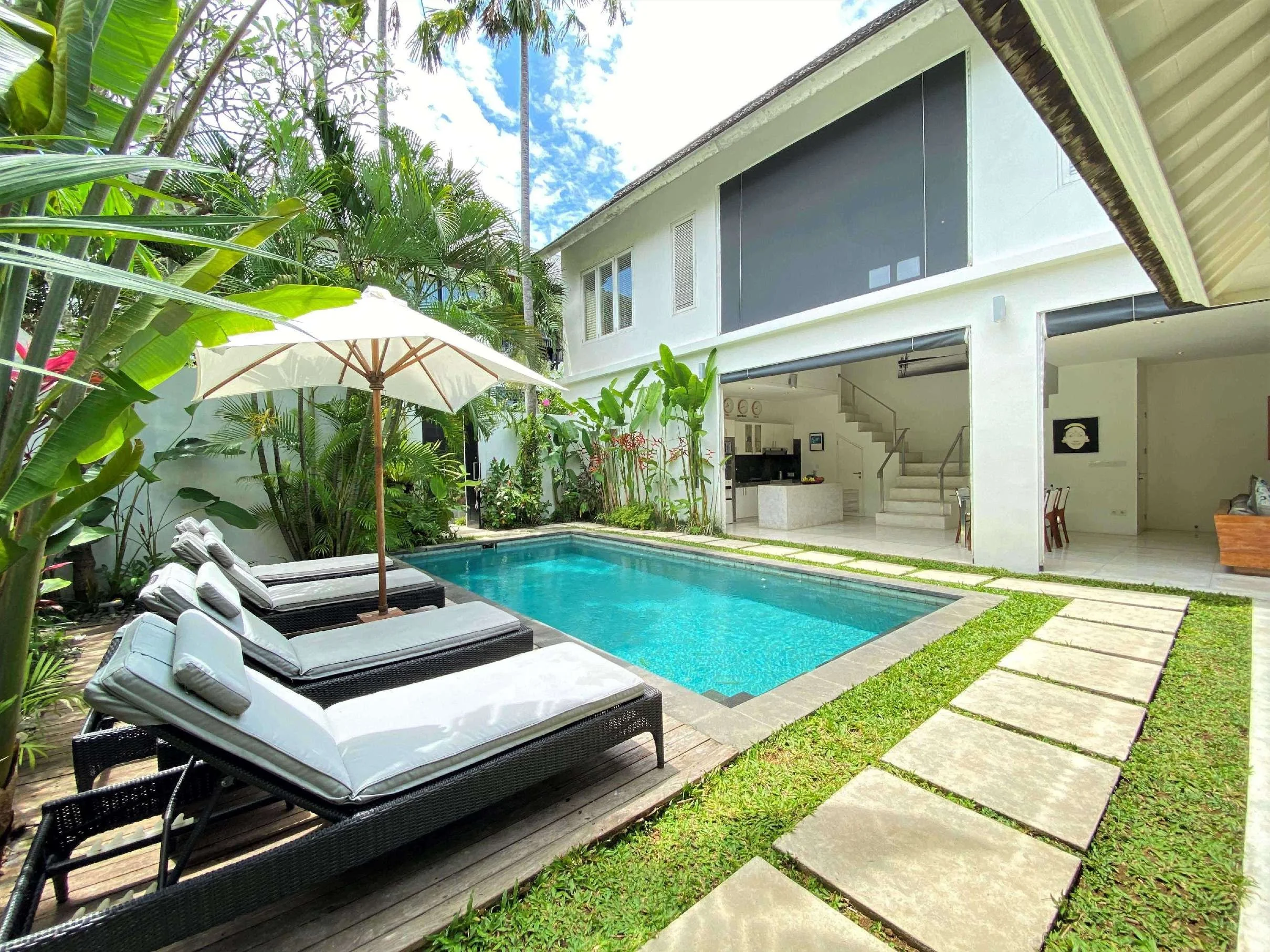 A modern house with a swimming pool in the backyard, surrounded by lush greenery and lounge chairs with an umbrella.