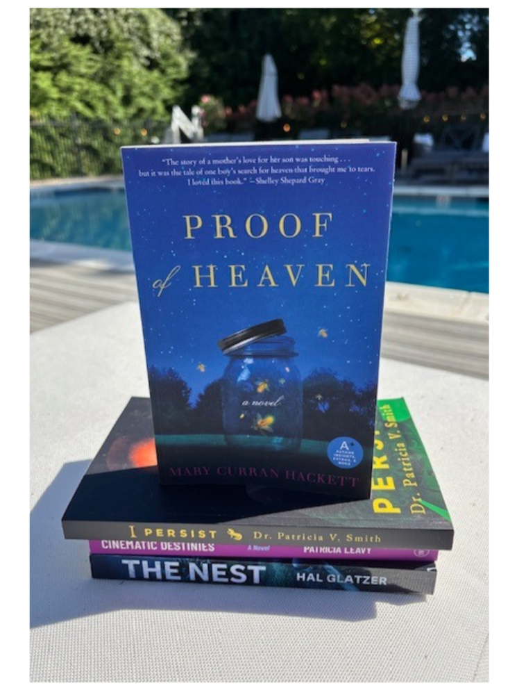 Stack of books beside a pool with Proof of Heaven by Mary Curran Hackett on top, featuring its starry cover and glowing jar artwork, highlighting the bestselling novel's luxury hotel partnership with Bedside Reading.