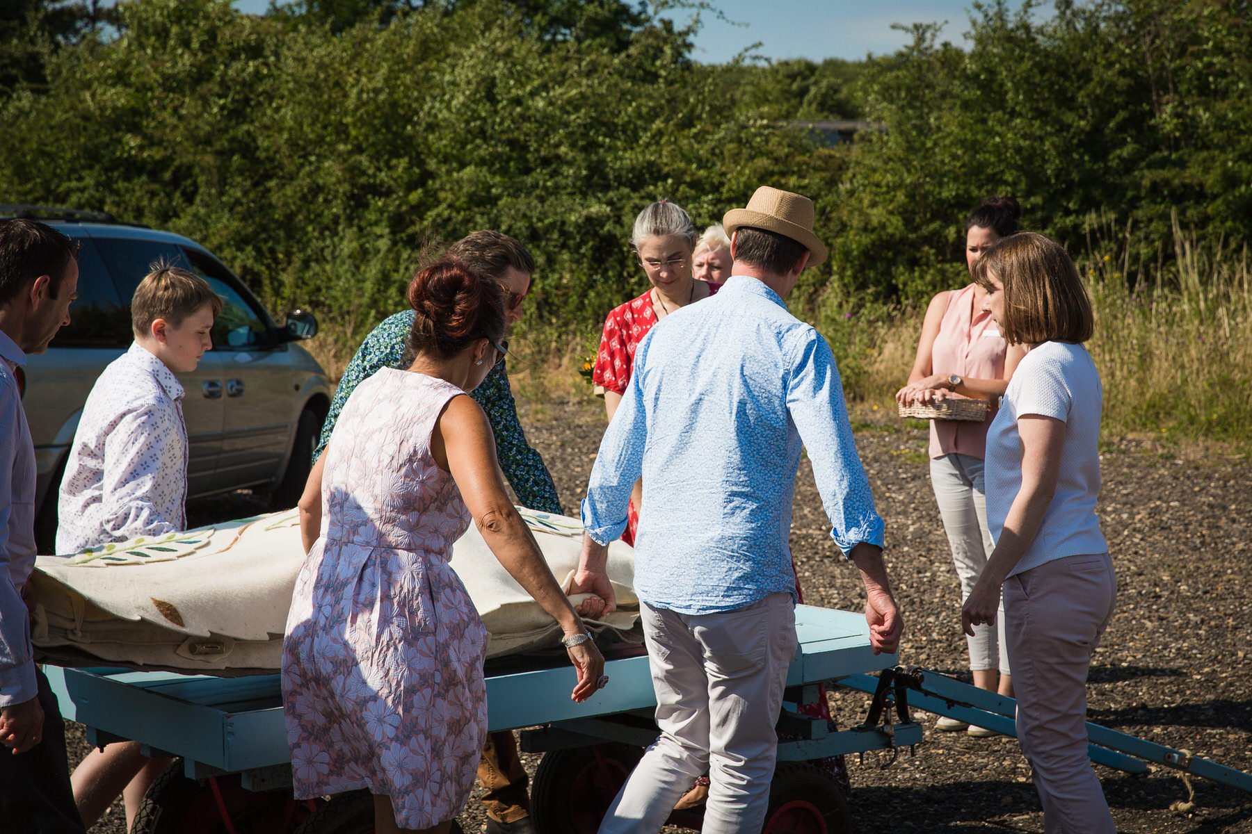 Family lifting a woollen shroud from the funeral car onto a cart at Clandon Wood natural burial ground in Surrey.