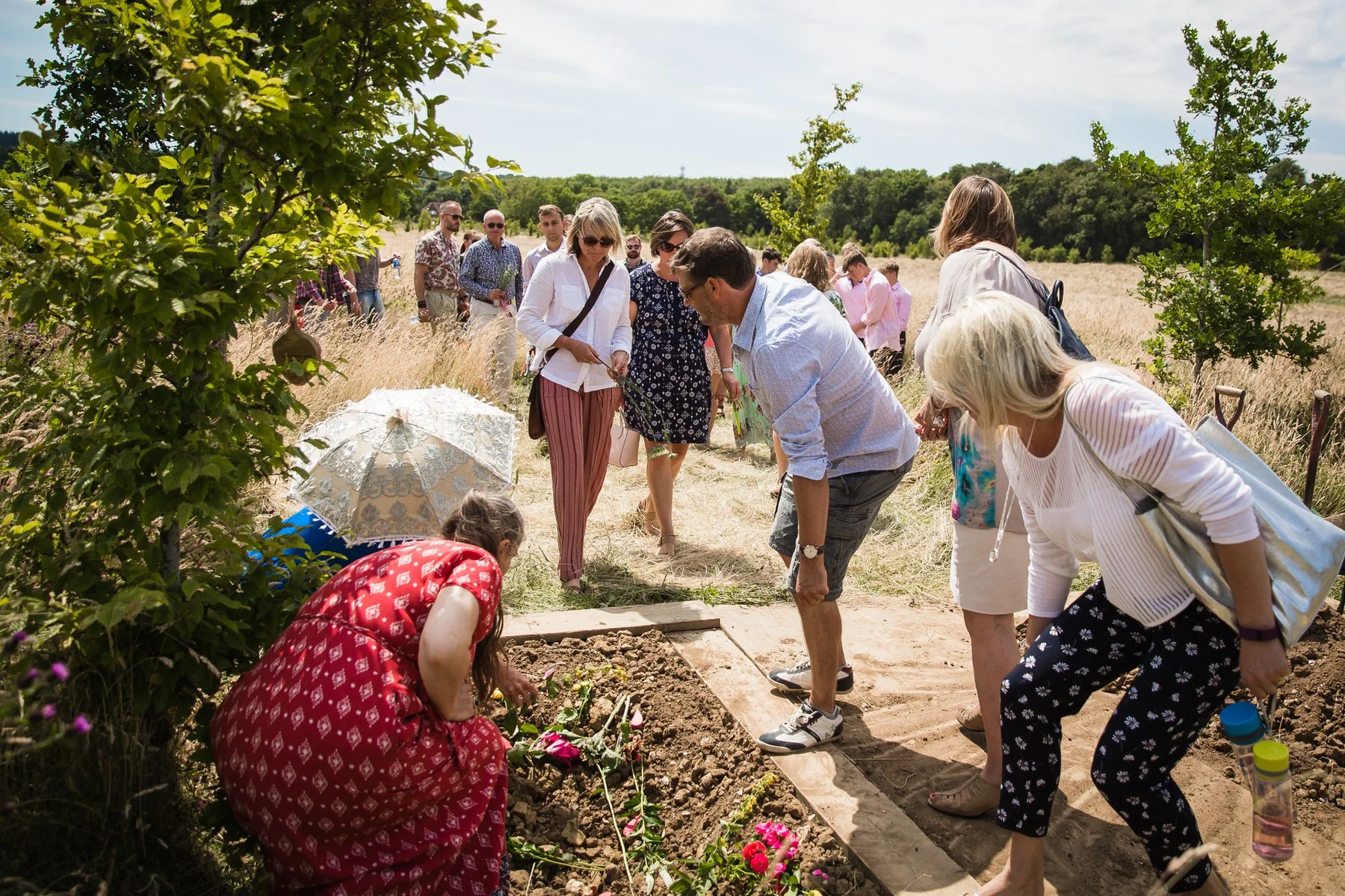 Friends and family gathered around a natural burial grave at Clandon Wood, laying flowers and red hearts with messages on Rory’s grave.