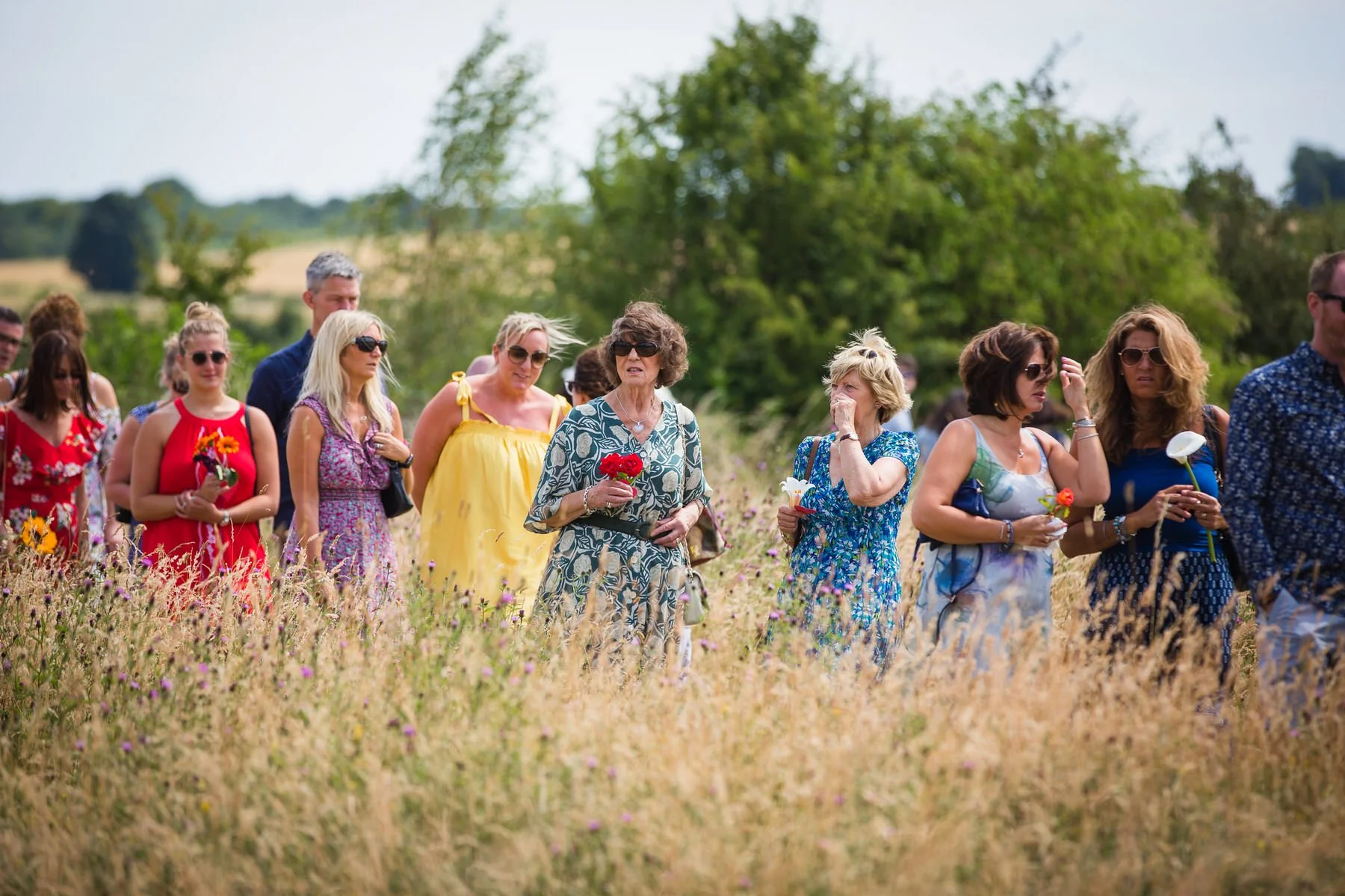 Mourners holding flowers in a wildflower meadow at Clandon Wood natural burial ground