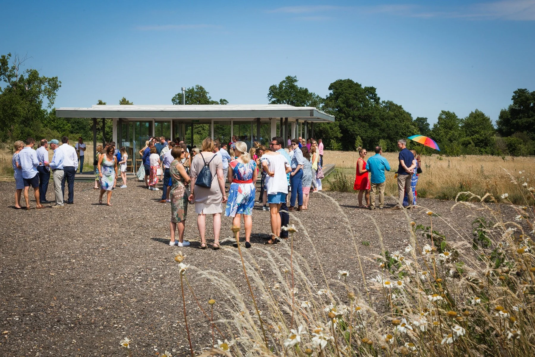 Guests arriving and greeting each other inside the glass pavilion at Clandon Wood natural burial ground in Surrey.