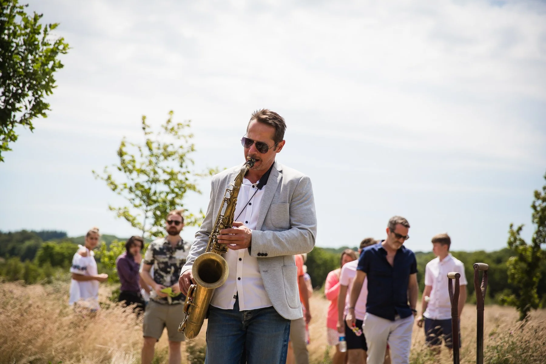 Saxophonist leading a long line of family and friends through the meadow back to the graveside at Clandon Wood natural burial ground in Surrey.