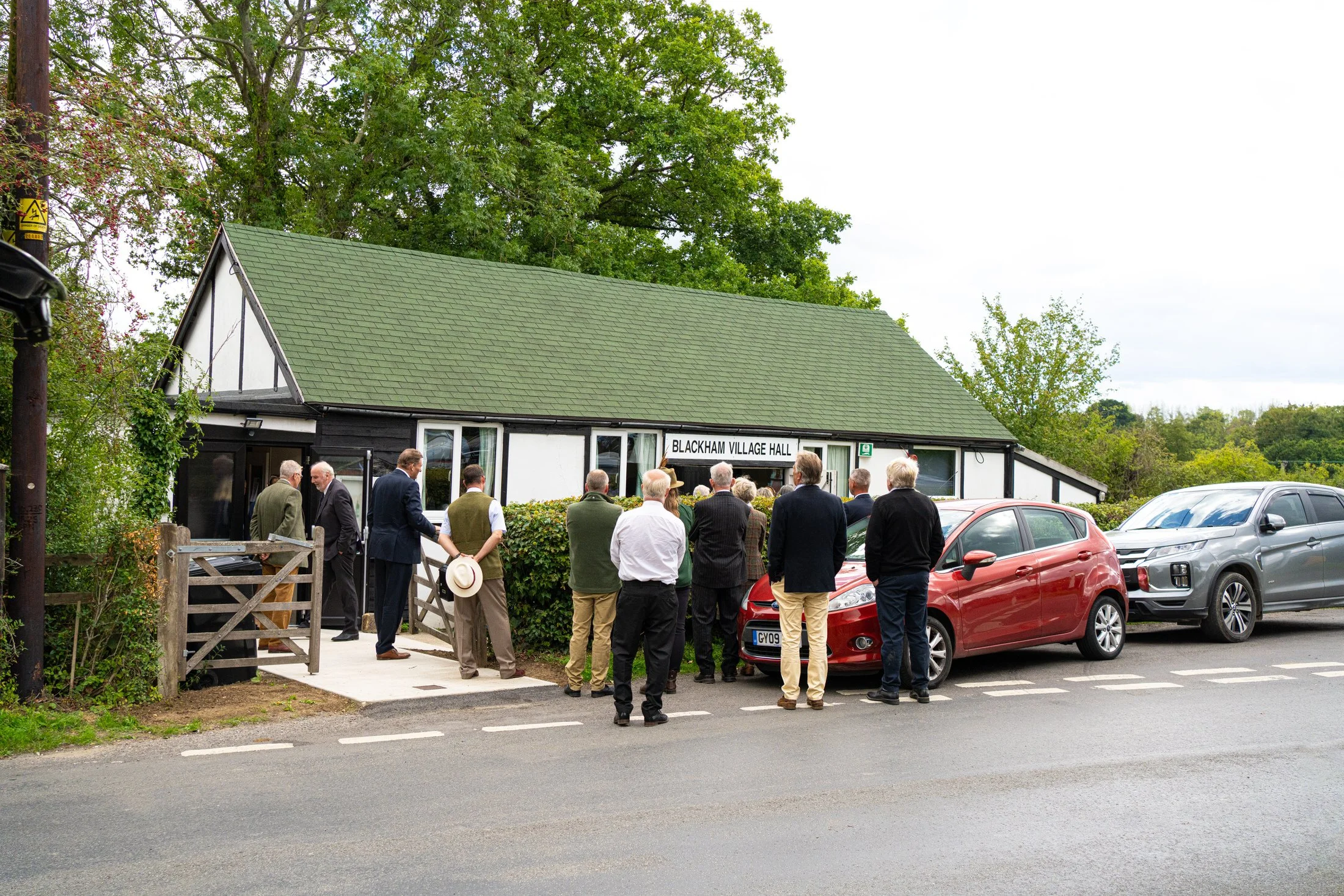Mourners arriving at a hall used as a funeral overflow room, with live screens and sound by UK Funeral Video Services