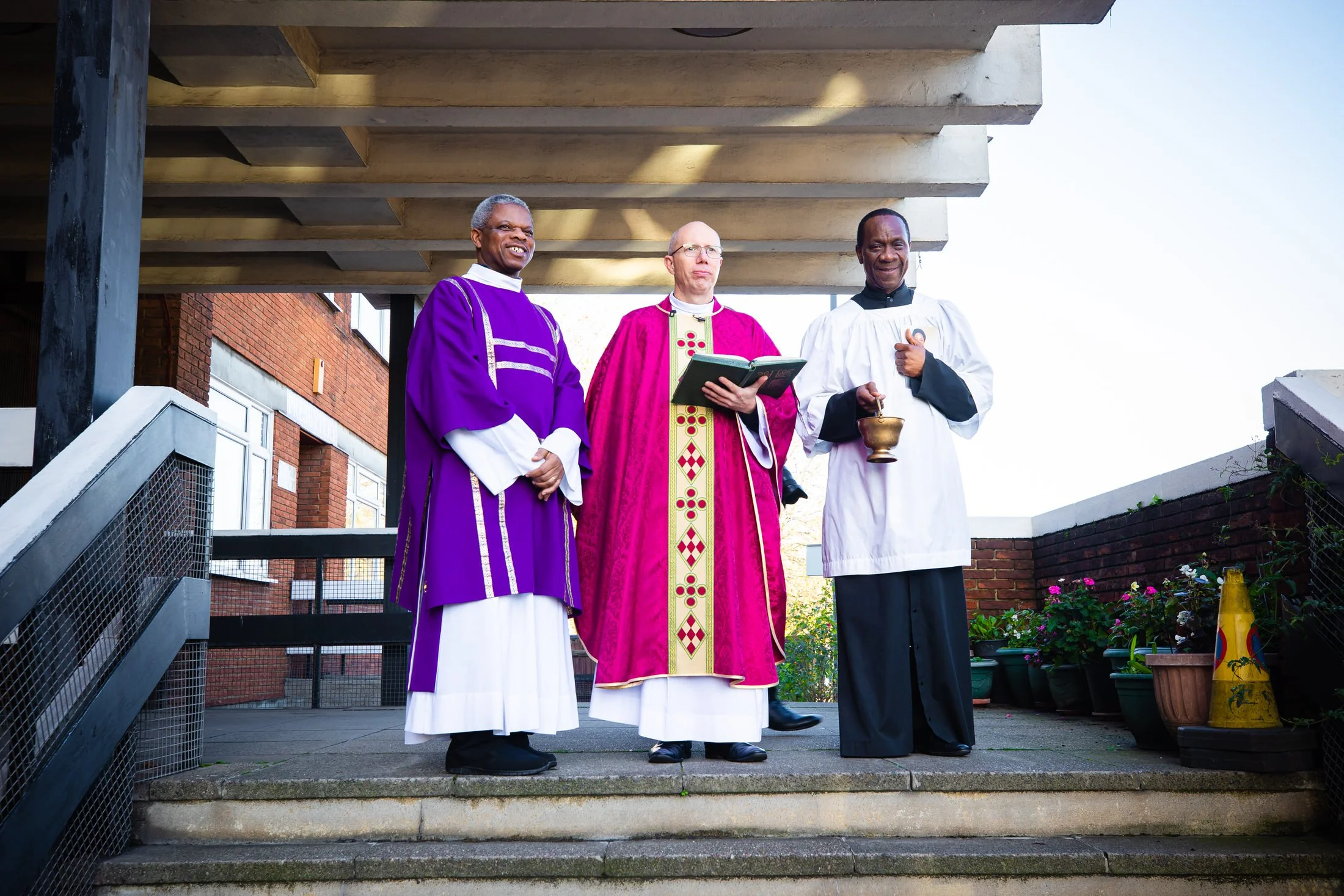 Three priests waiting on the church steps in London before a funeral, photographed by funeral photographer Shaun Foulds