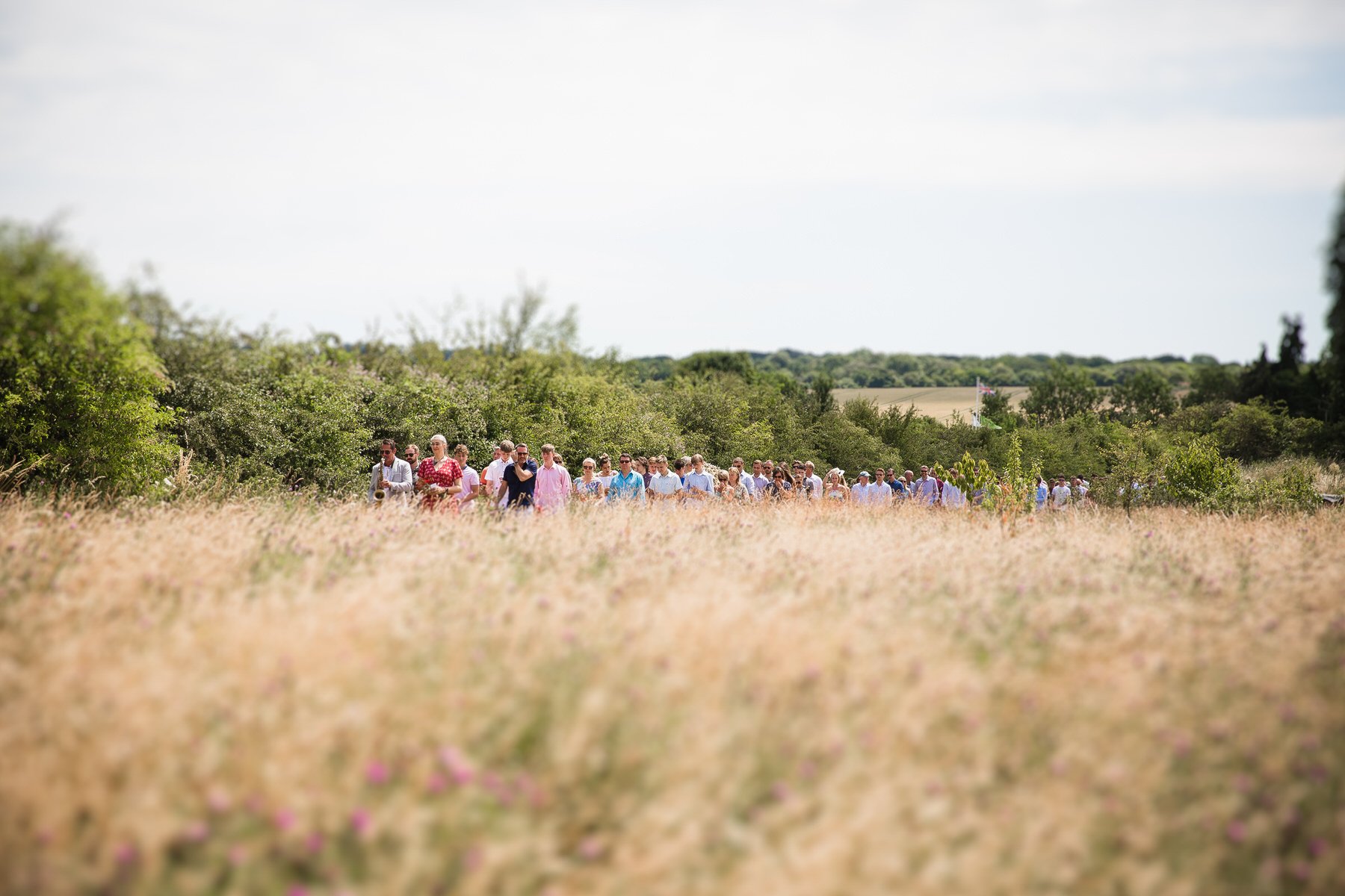 Saxophonist leading a long line of family and friends through the meadow back to the graveside at Clandon Wood natural burial ground in Surrey.
