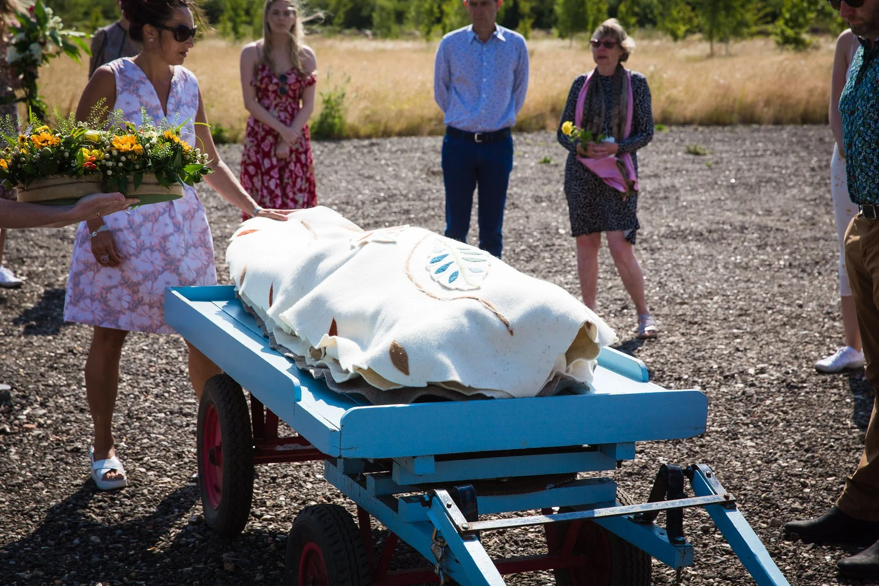 Family lifting a woollen shroud from the funeral car onto a cart at Clandon Wood natural burial ground in Surrey.