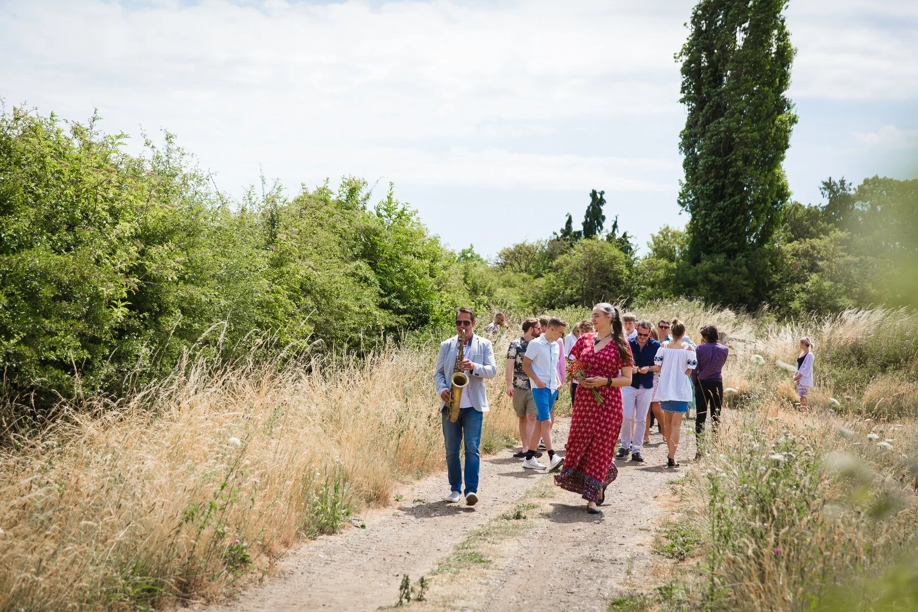 Saxophonist leading a long line of family and friends through the meadow back to the graveside at Clandon Wood natural burial ground in Surrey.