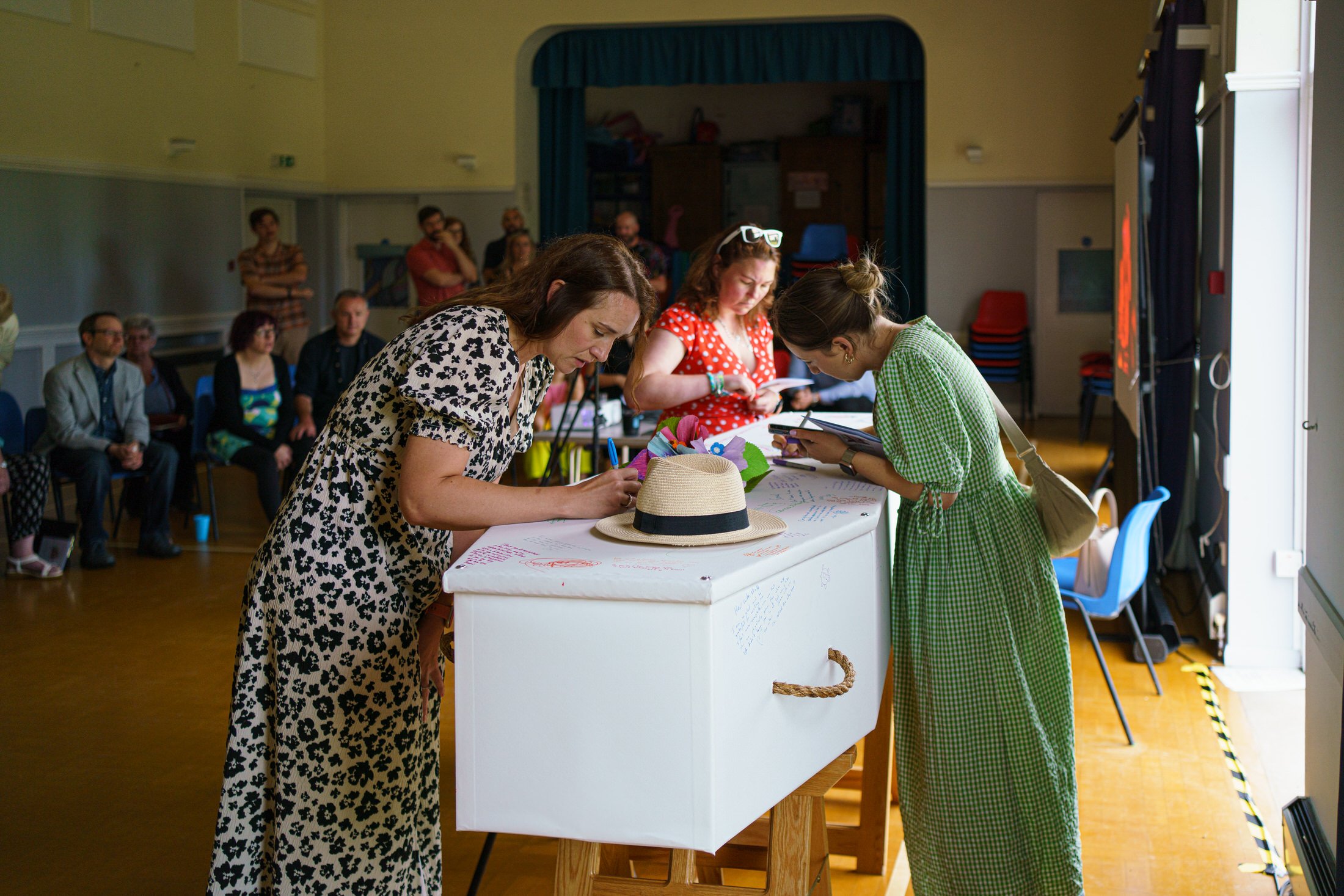 Mourners writing messages on a white coffin at a celebration of life, captured during funeral filming