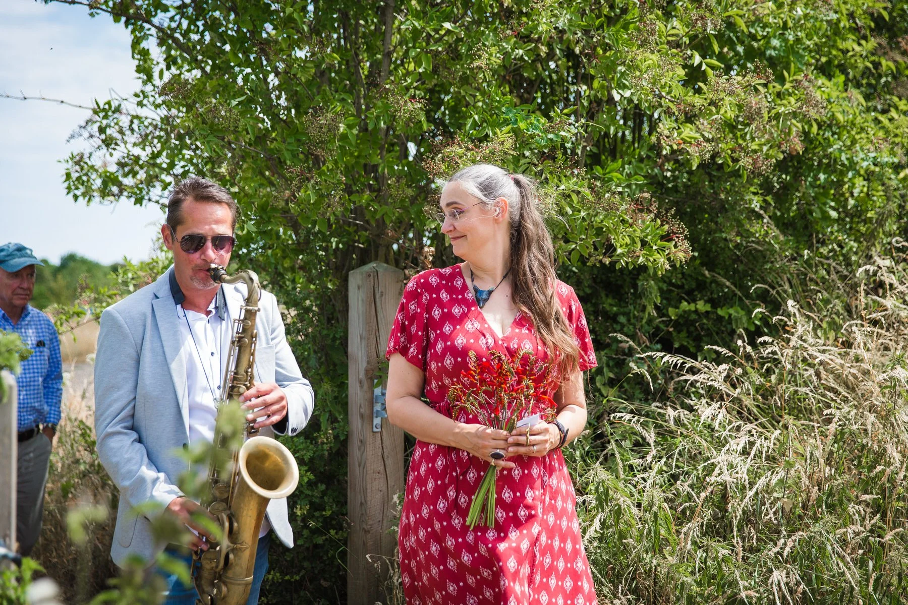 Saxophonist leading a long line of family and friends through the meadow back to the graveside at Clandon Wood natural burial ground in Surrey.