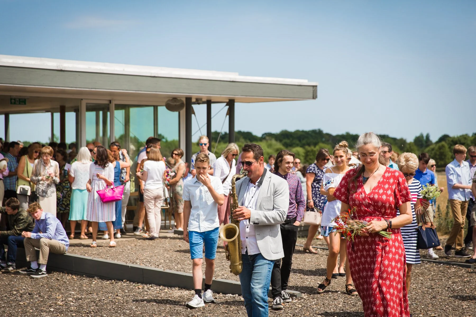 Saxophonist leading a long line of family and friends through the meadow back to the graveside at Clandon Wood natural burial ground in Surrey.