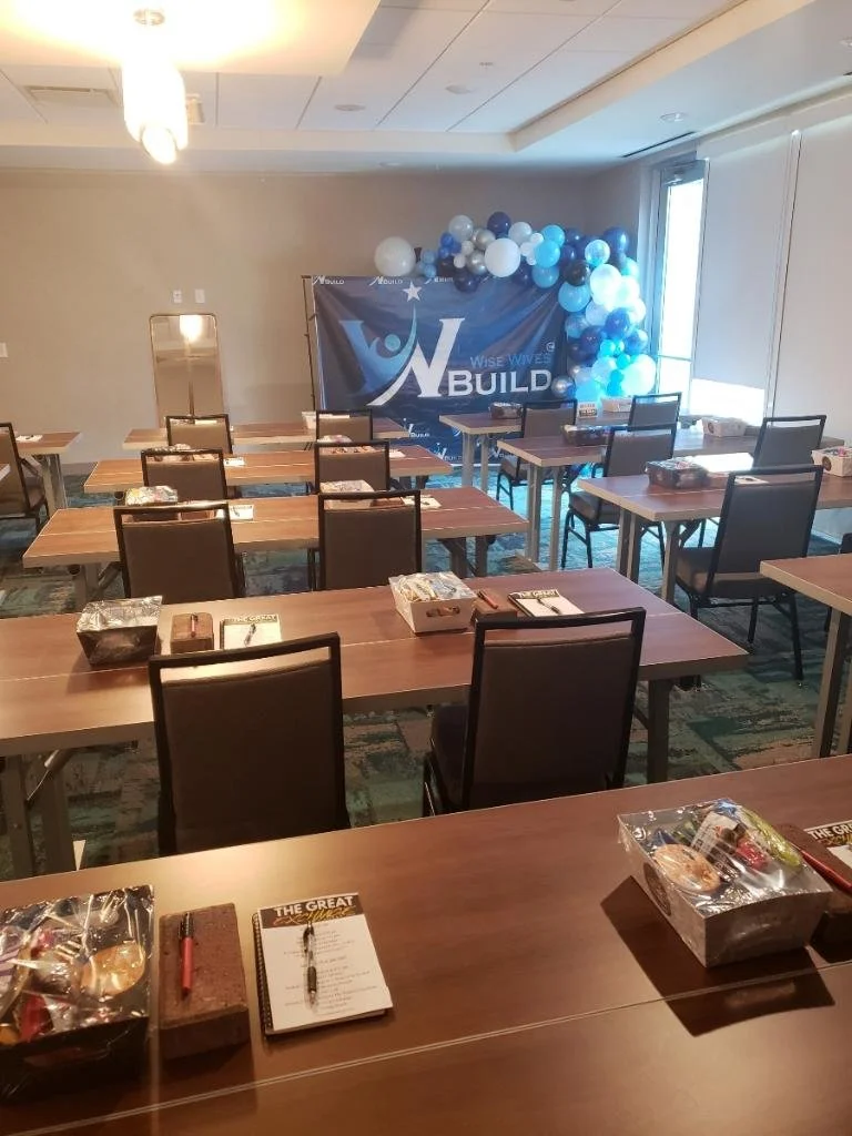 Conference room set up with tables, chairs, and a banner reading 'Build' with a cluster of blue and white balloons in the corner.