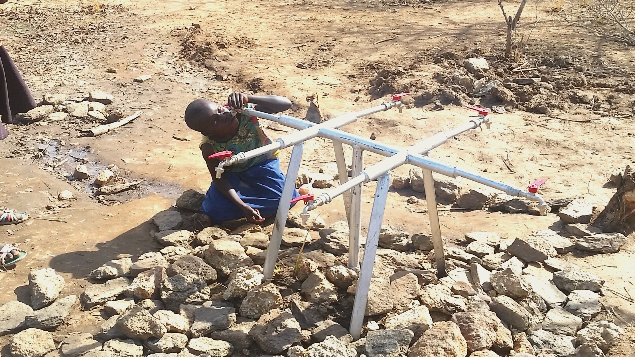 This young girl desperately sucks on an empty water pipe, as Imvepi Camp goes on two long days without any water.