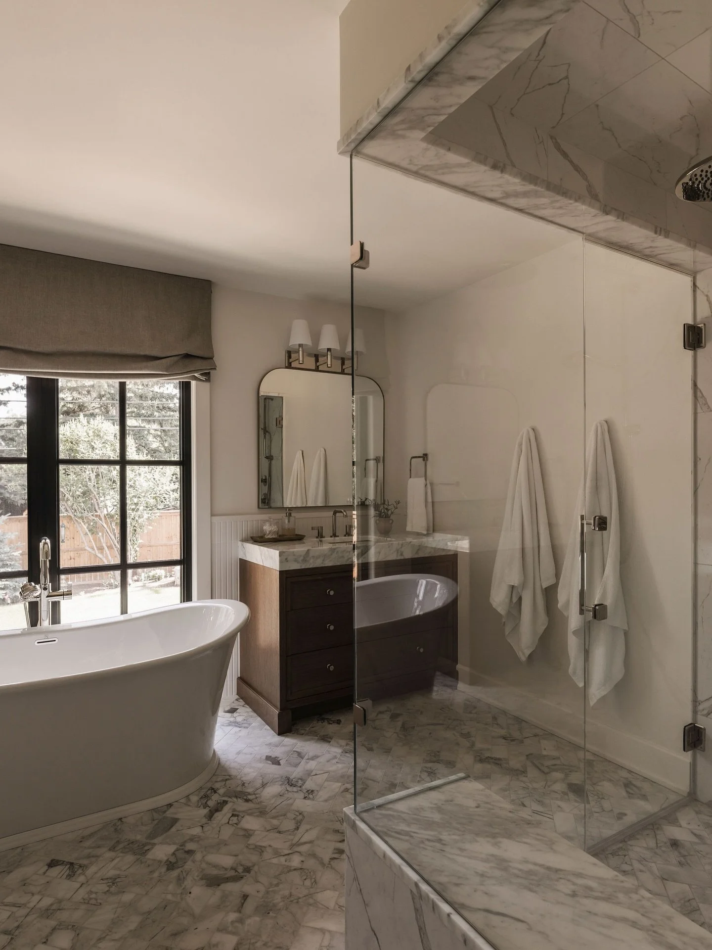 A calm and timeless, primary bathroom filled with warm textures, soft light, and intentional details. Marble with movement, wood that grounds the space, and a sculptural soaking tub positioned to take in the beautiful backyard views. Every element wa