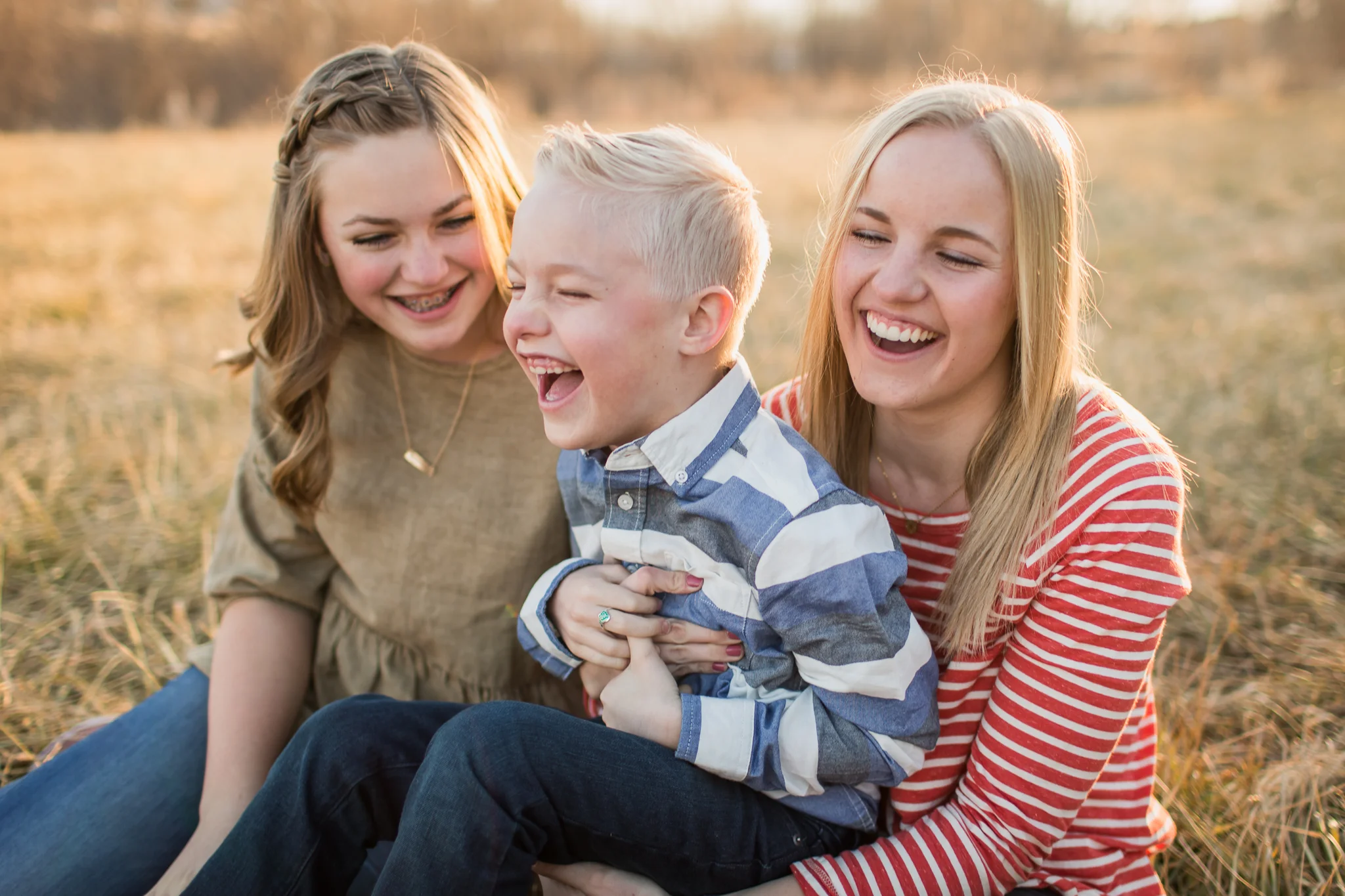 Sisters and brother laughing sitting in grass.