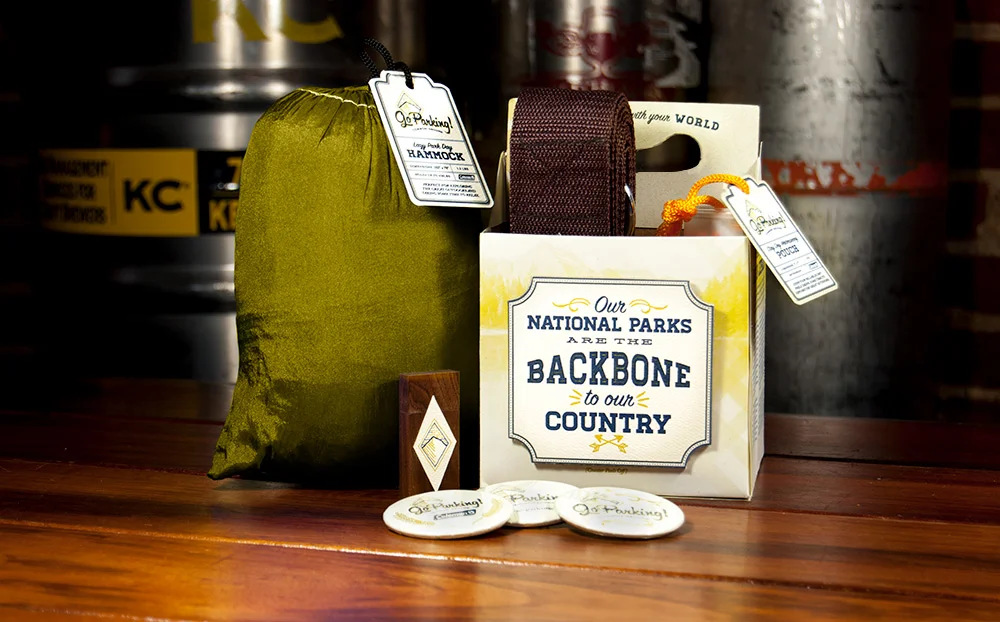 The promotion includes a travel hammock, straps, a waterproof pouch, wooden USB, and promotional pins all nestled within a 4-pack beer container. 