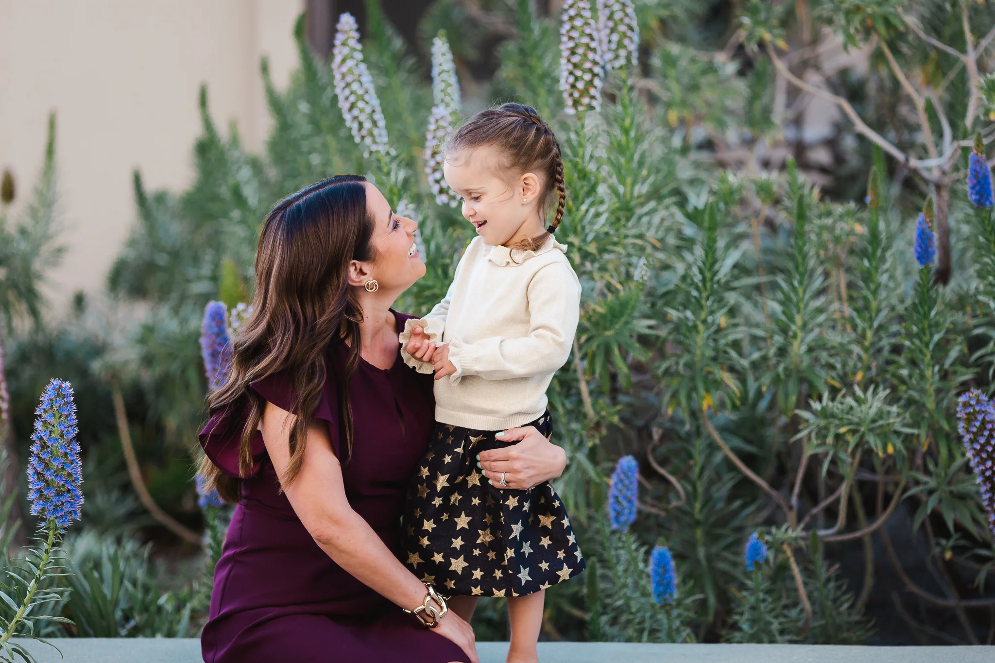 mother and young daughter looking loving at each other surrounded by beautiful purple flowers in La Jolla, California.