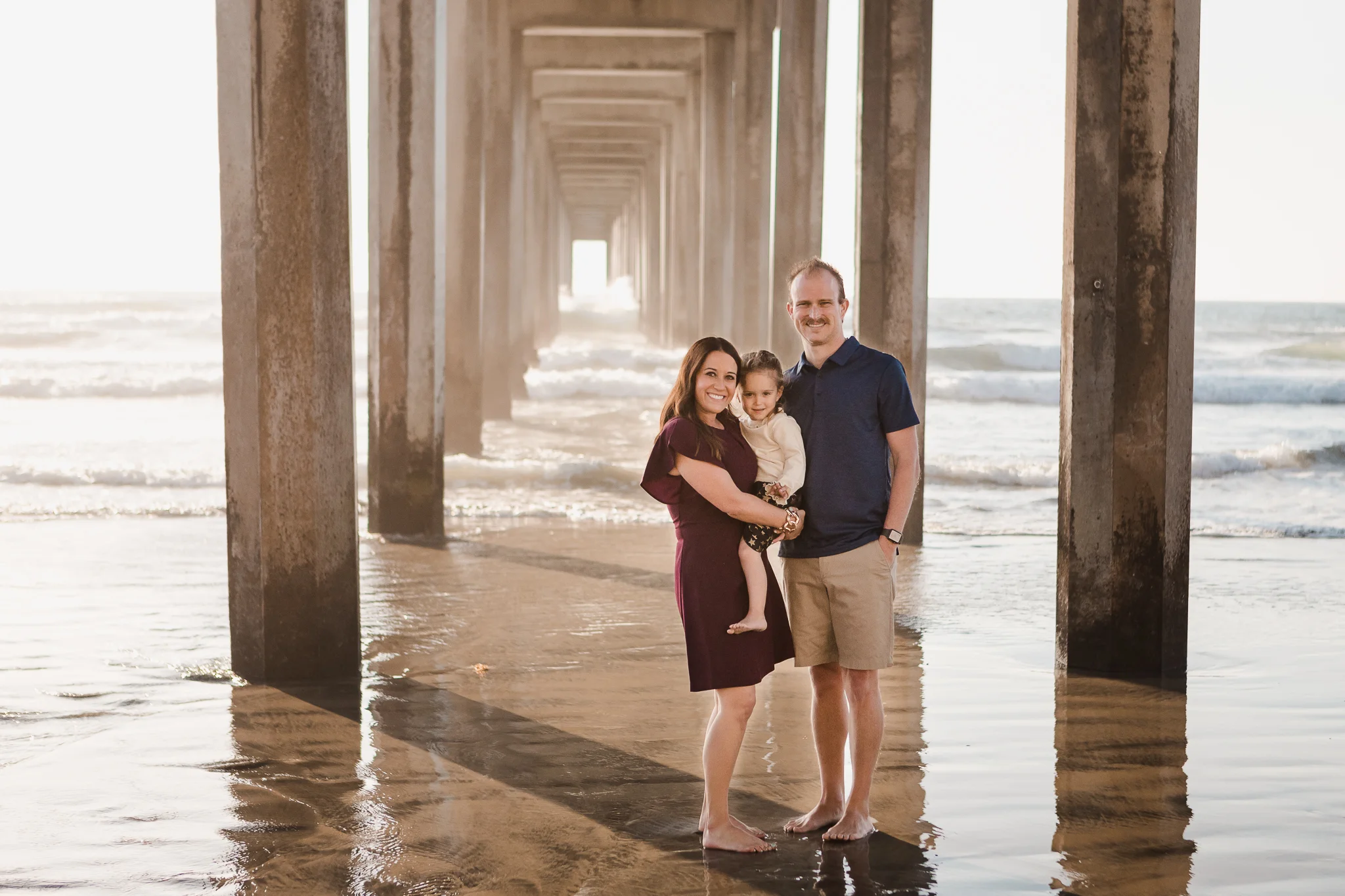 family of three together at the beach under Scripps Pier in La Jolla, CA