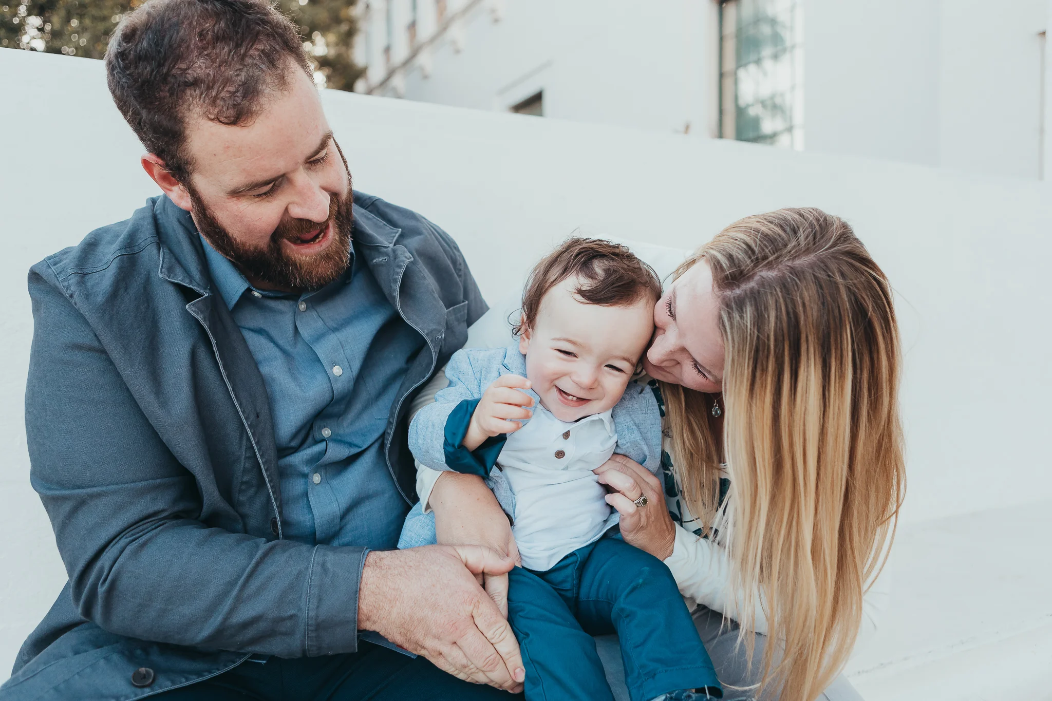 DAD AND MOM SNUGGLING 1 YEAR OLD BABY BOY WHILE HE LAUGHS.