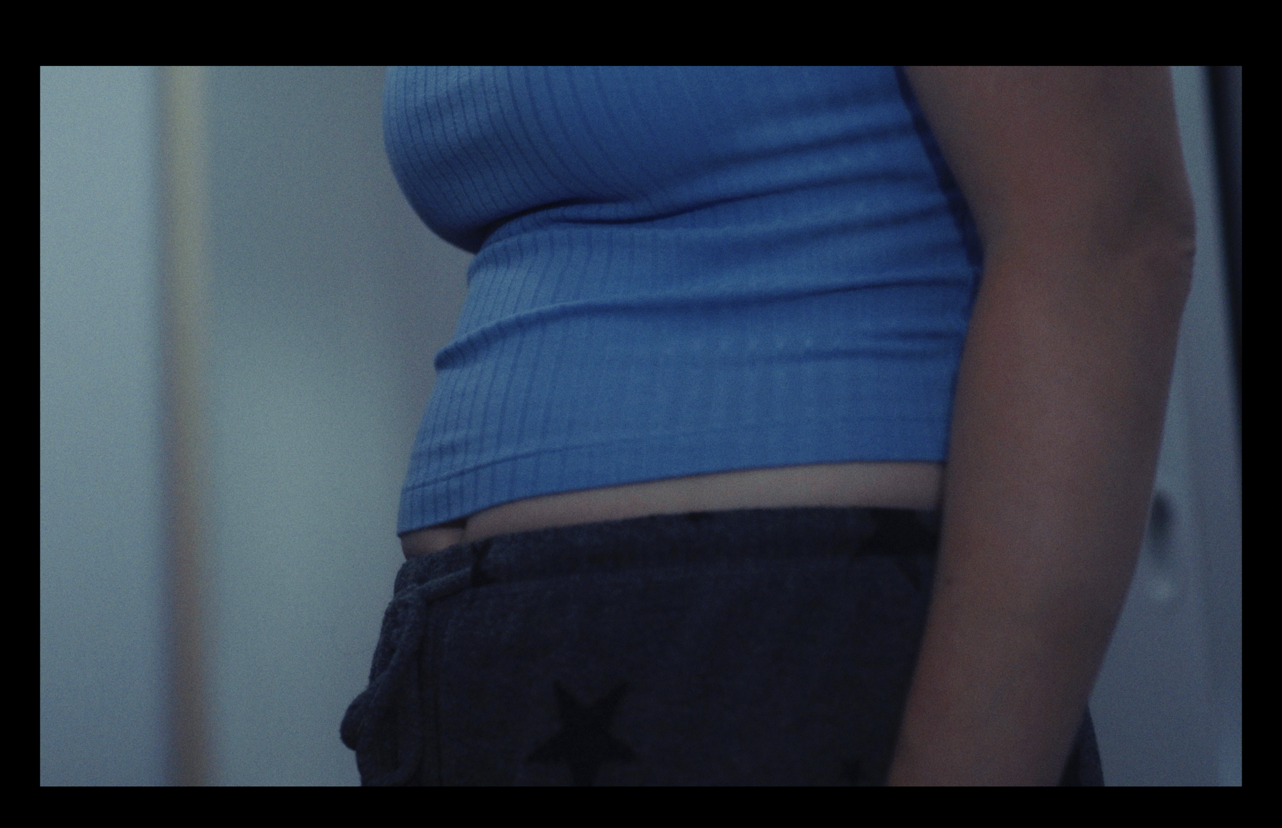 Close-up of a person's midsection, wearing a blue ribbed short-sleeved shirt and dark shorts.