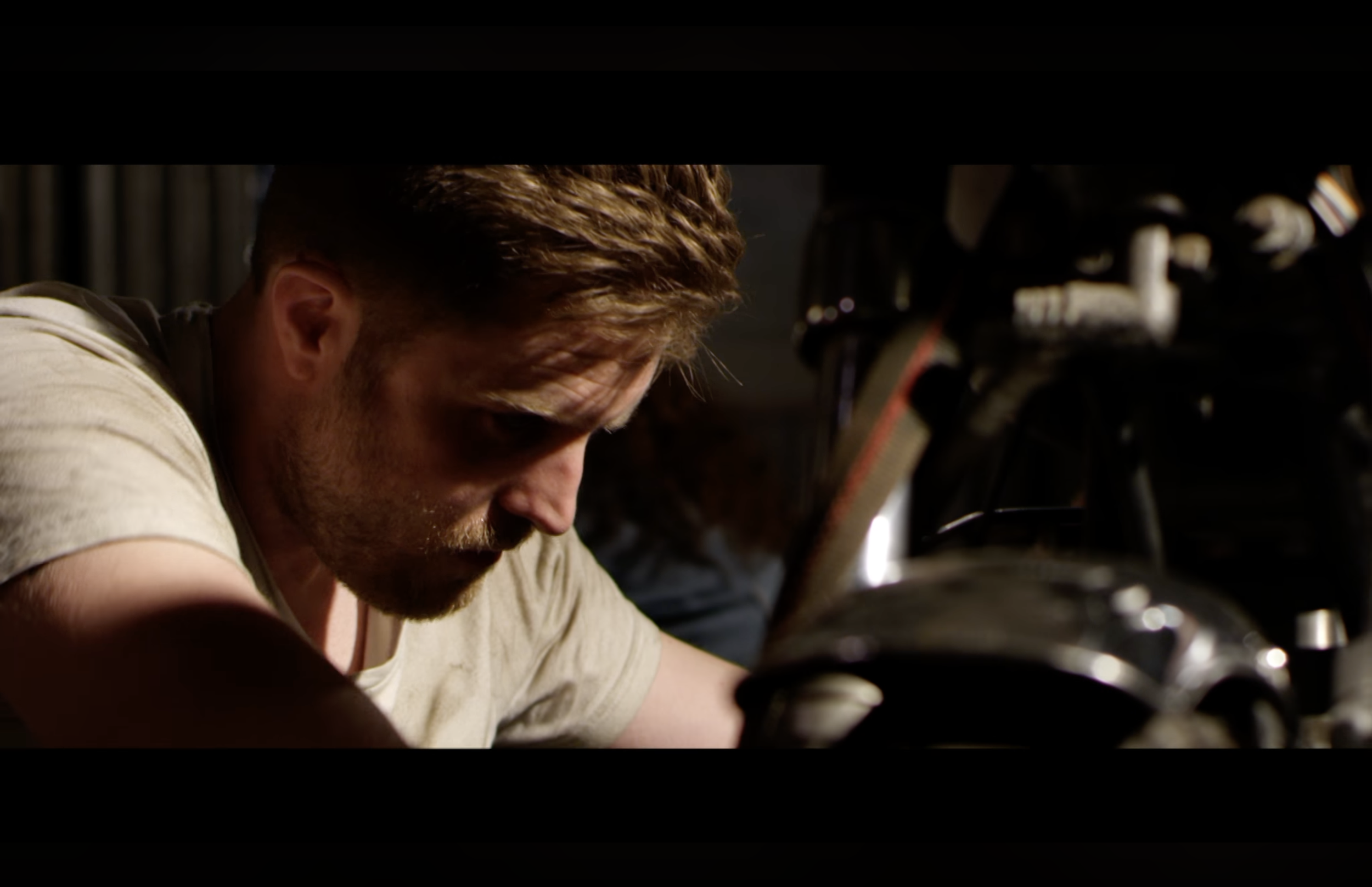 Close-up of a man with reddish hair and a beard working with a motorcycle.